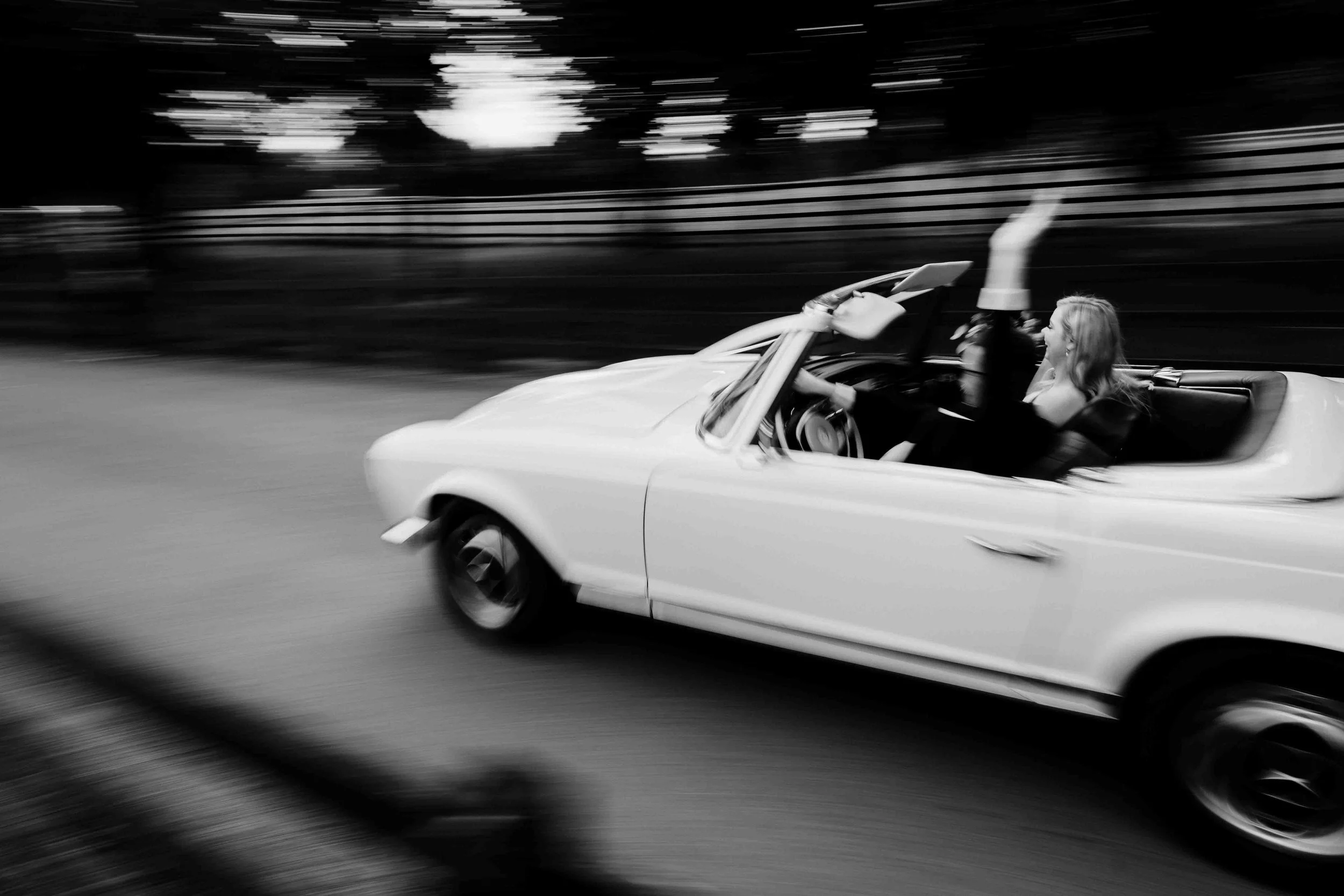 black and white wedding photo of couple in a car going so fast it's blurred