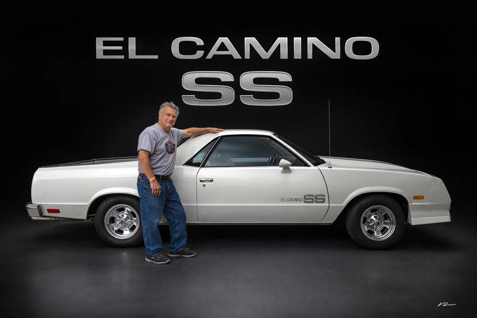 A man standing next to a classic white Chevrolet El Camino SS in a showroom with a black background and 'El Camino SS' sign overhead.