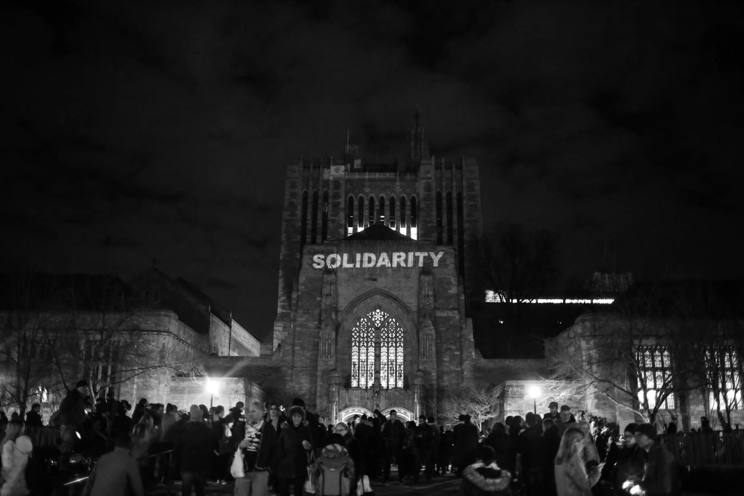 New Haven, Connecticut - January 29th, 2017: A vigil is held for immigrants and refugees in front of Yale's Sterling Memorial Library. A projection onto the library reads "Solidarity".