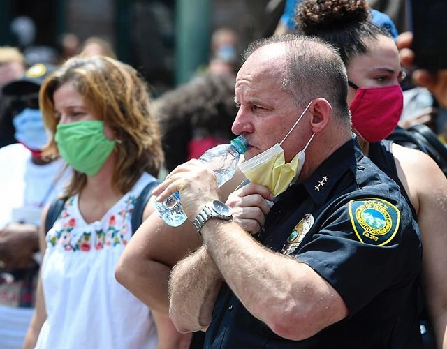 Asheville Police Chief David Zack takes a sip of water as temperatures creep into the 90&rsquo;s while Asheville city officials, including Mayor Esther Manheimer, left, listen to speakers in front of the Asheville Police Department June 6, 2020. 📷@a