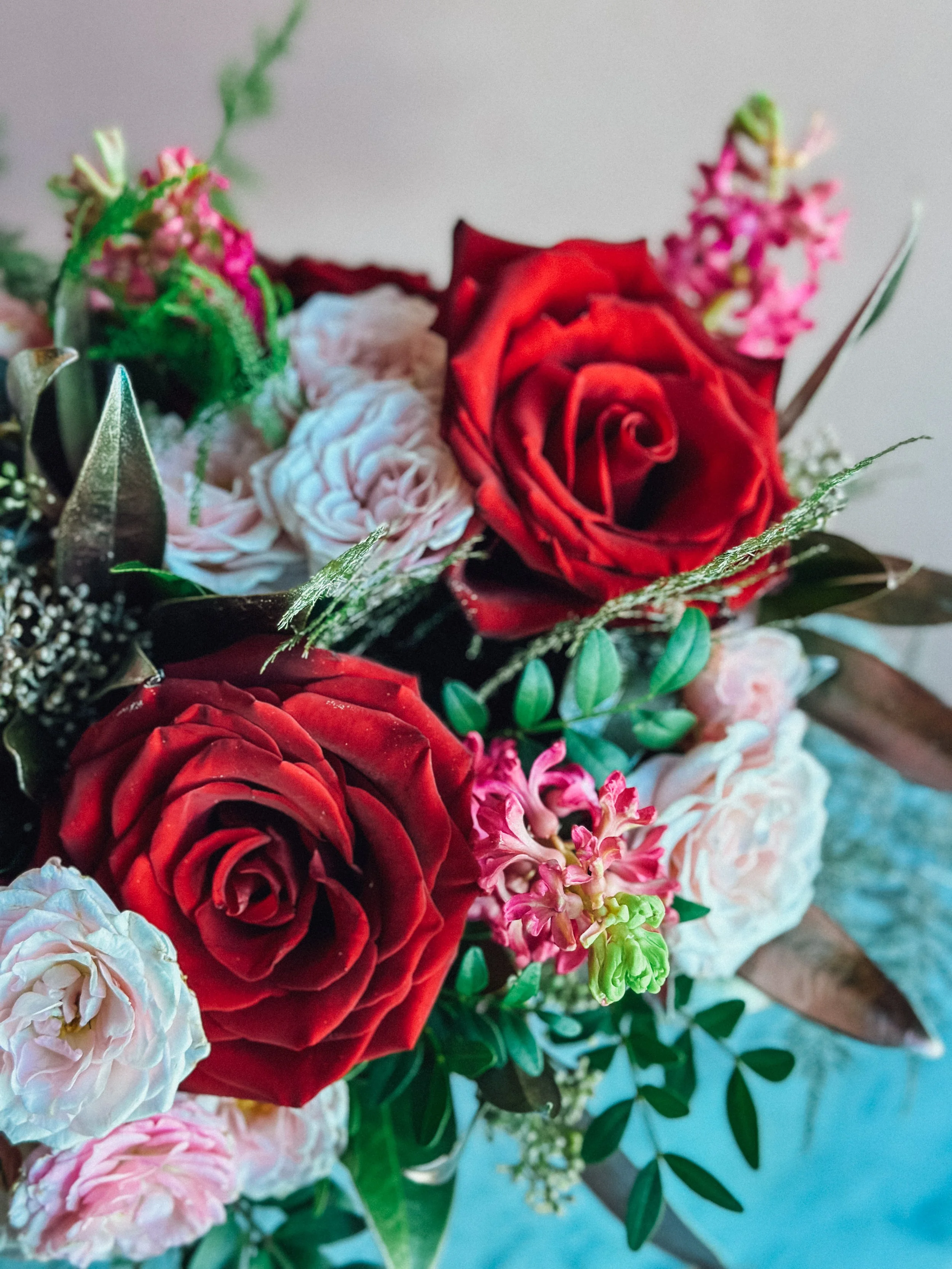 Small Valentine’s Day flower arrangement with red roses, pink tulips, blue accents, and fresh greenery in a red cube vase, available for Edmonton St Albert and Sturgeon County flower delivery.
