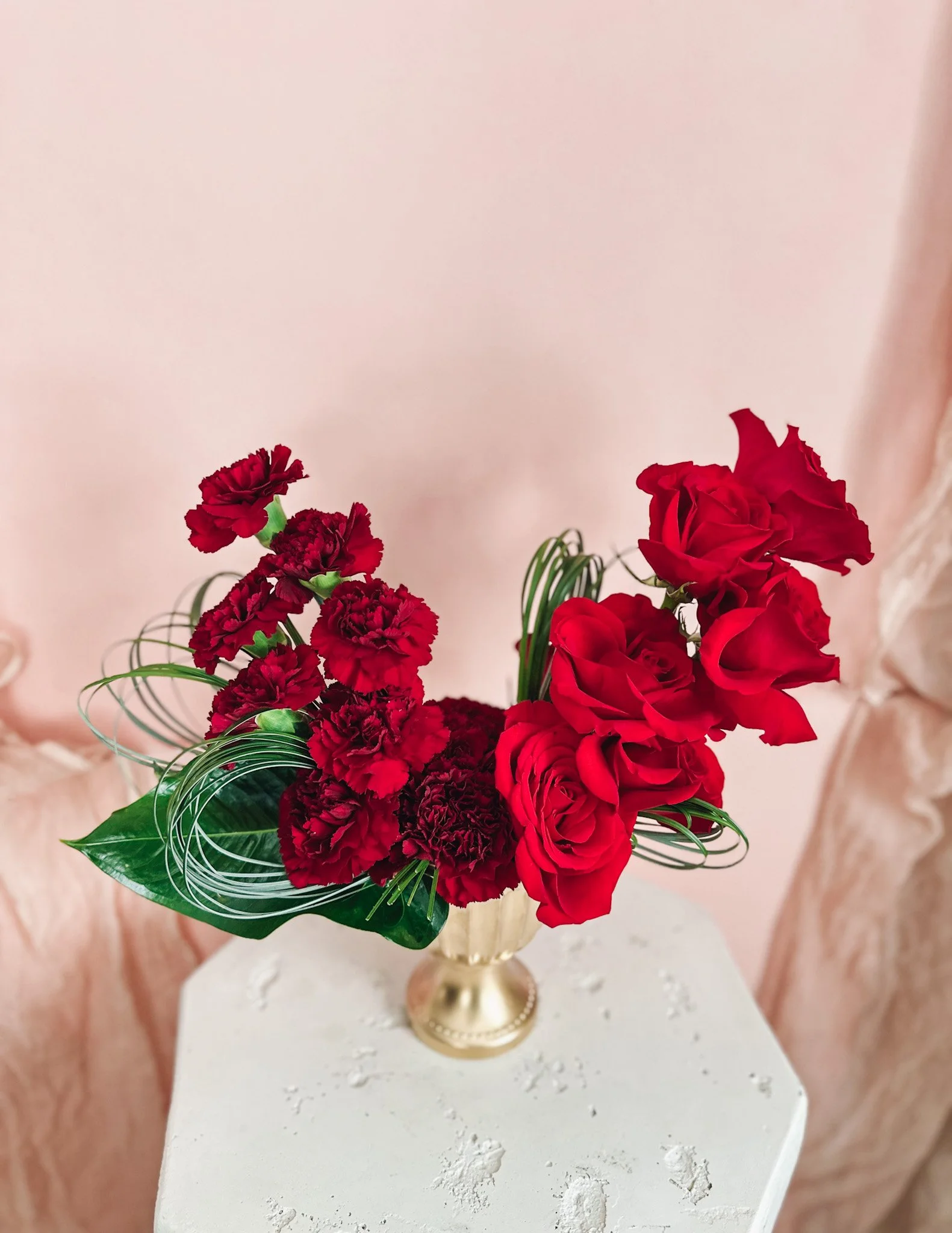 Tall Valentine’s Day floral arrangement featuring stacked red roses and deep crimson carnations with sculptural greenery in a gold pedestal vase, available for Edmonton flower delivery.