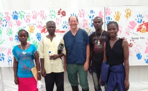 Dr. Daniel Lucey, center, poses with Ebola survivors in Monrovia, Liberia, in front of a wall featuring the hand prints of survivors.