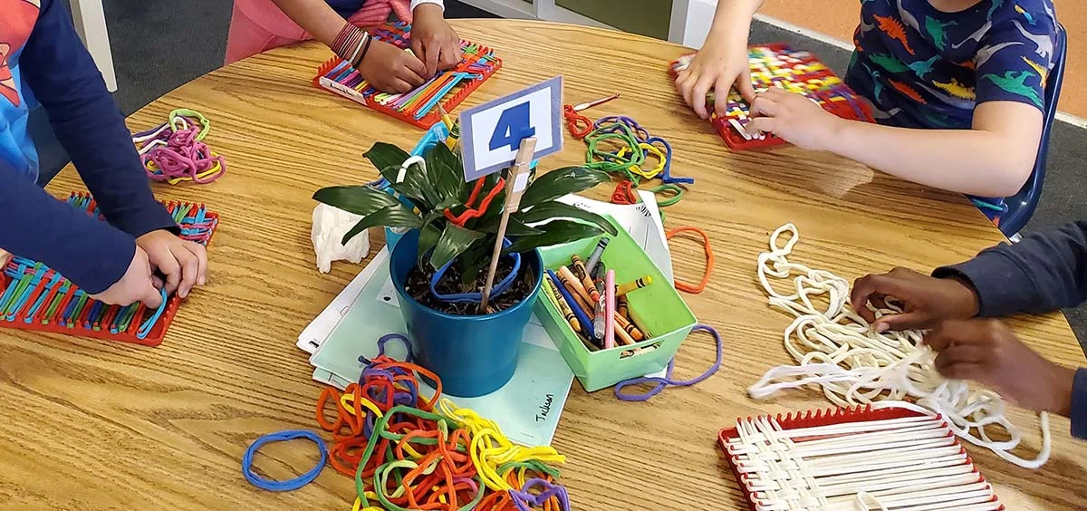 Kindergarten students learning the basics of weaving by making potholders.