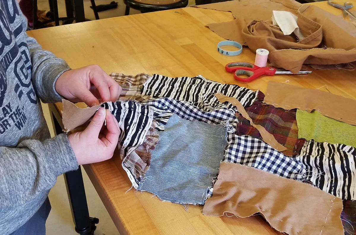 5th grader sewing fabric scraps together to make a quilt inspired by the work of the Gee’s Bend quilters.