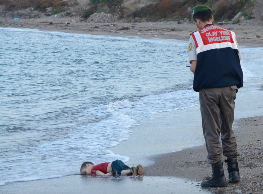 A Turkish police officer stands near of the drowned Syrian boy, 2015 @Reuters