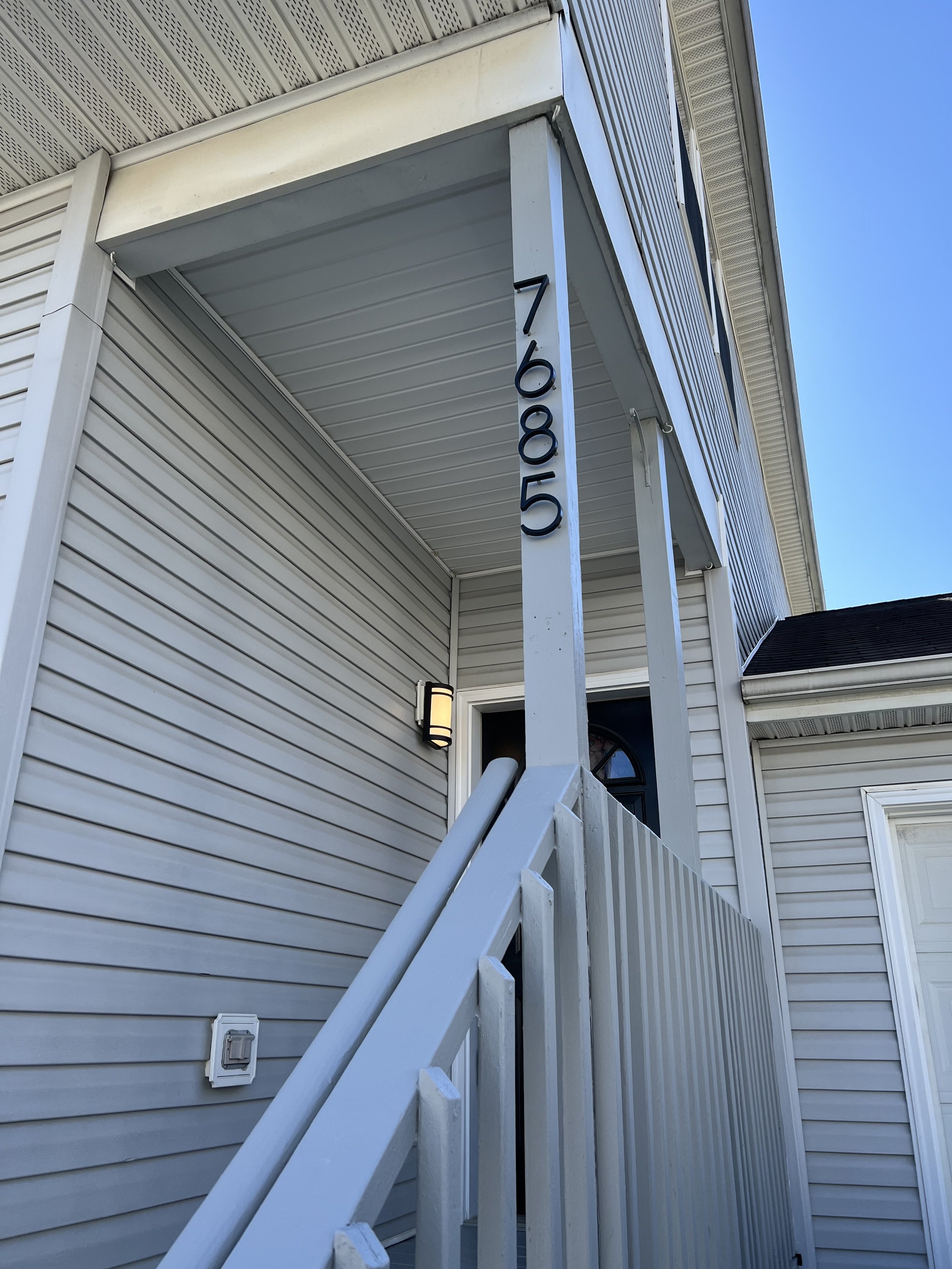 Freshly painted gray front porch column and railing beside house address numbers 7685