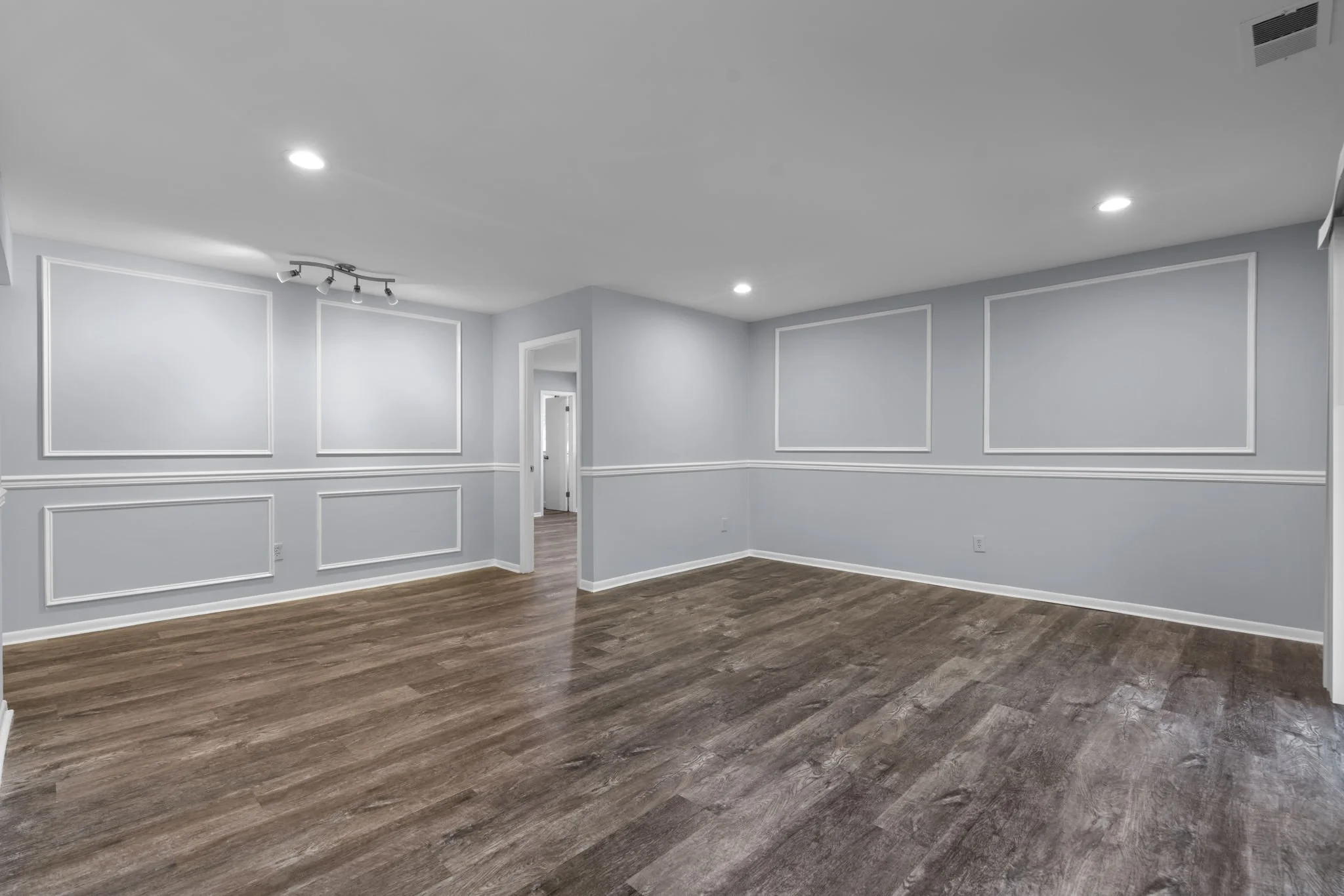 Renovated room with decorative wall paneling and picture-frame wainscoting added to gray walls, dark wood-look flooring