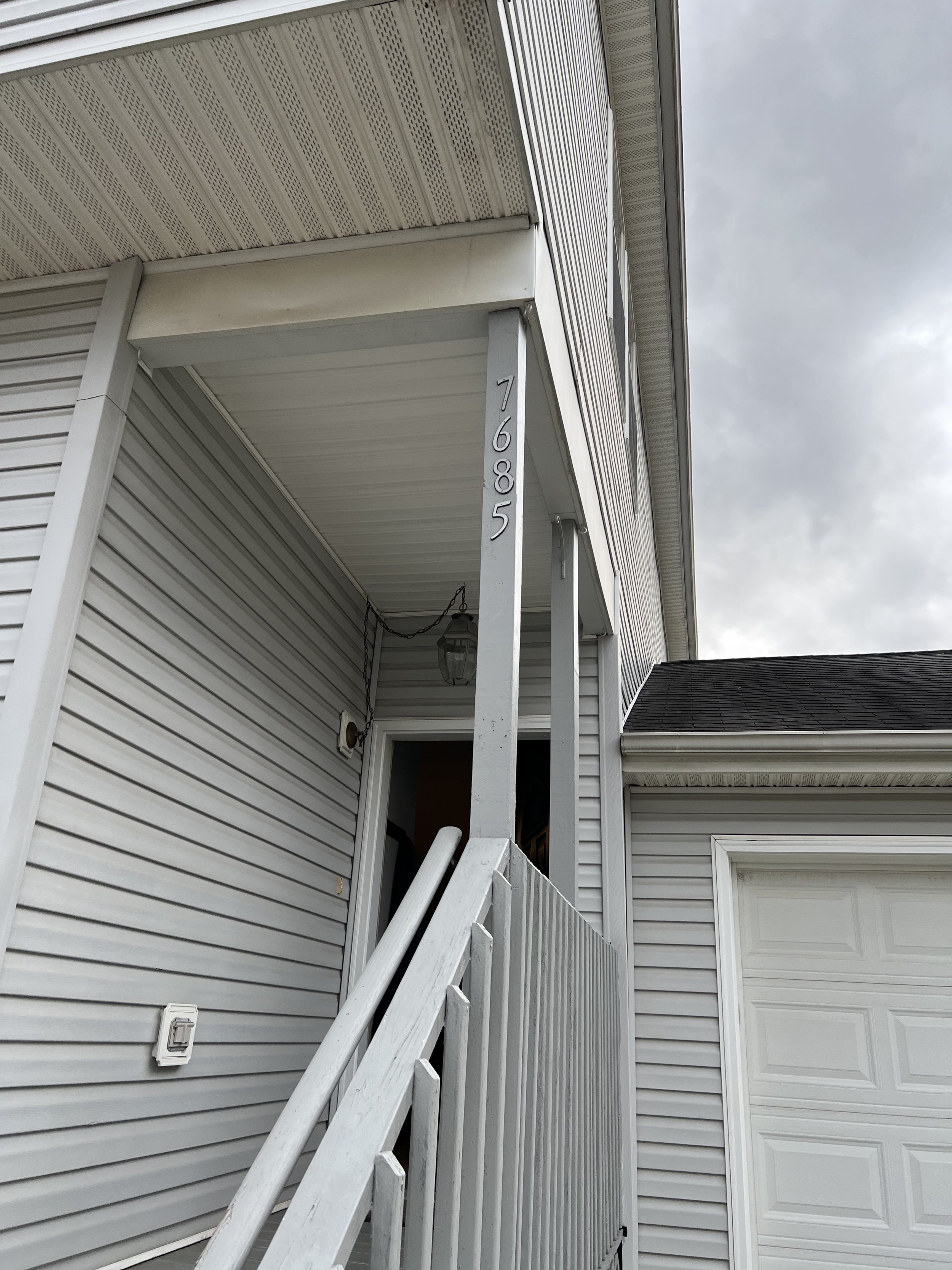 Front porch support column with peeling white paint next to house address numbers 7685