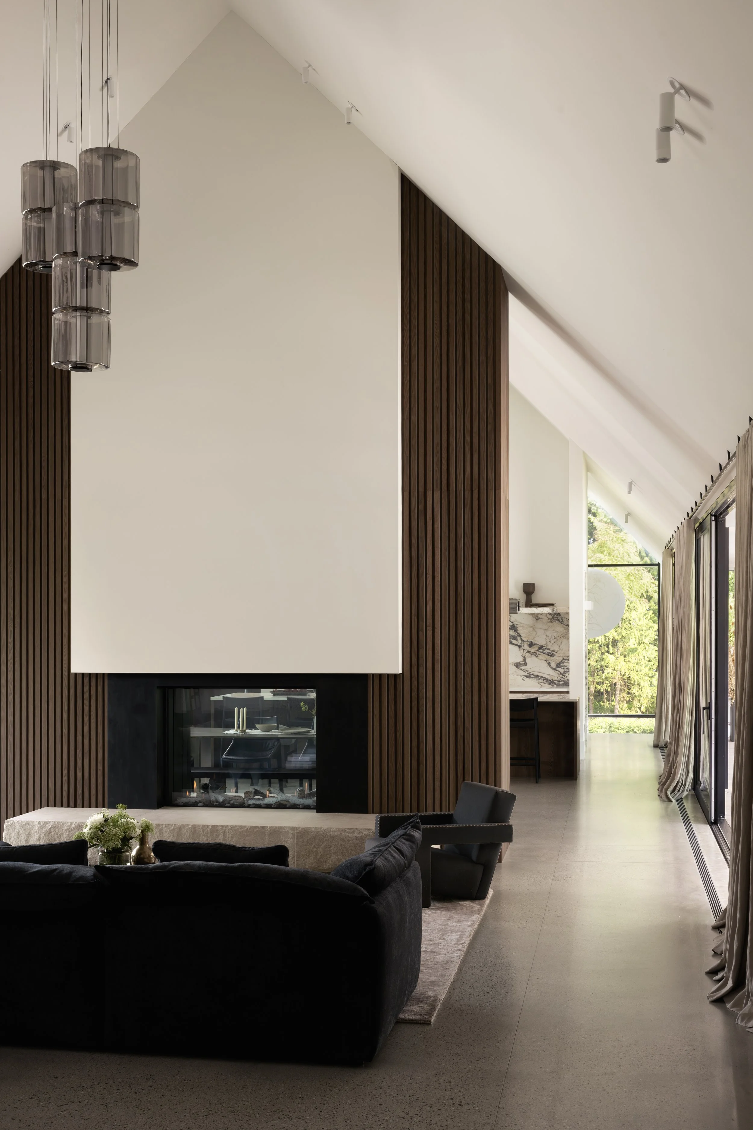  Connecting interior and landscape, the double-height living room unfolds toward the courtyard, where the vertical elegance of the   A-N-D Column Pendant by Lukas Peet reinforces the home's architectural scale. 