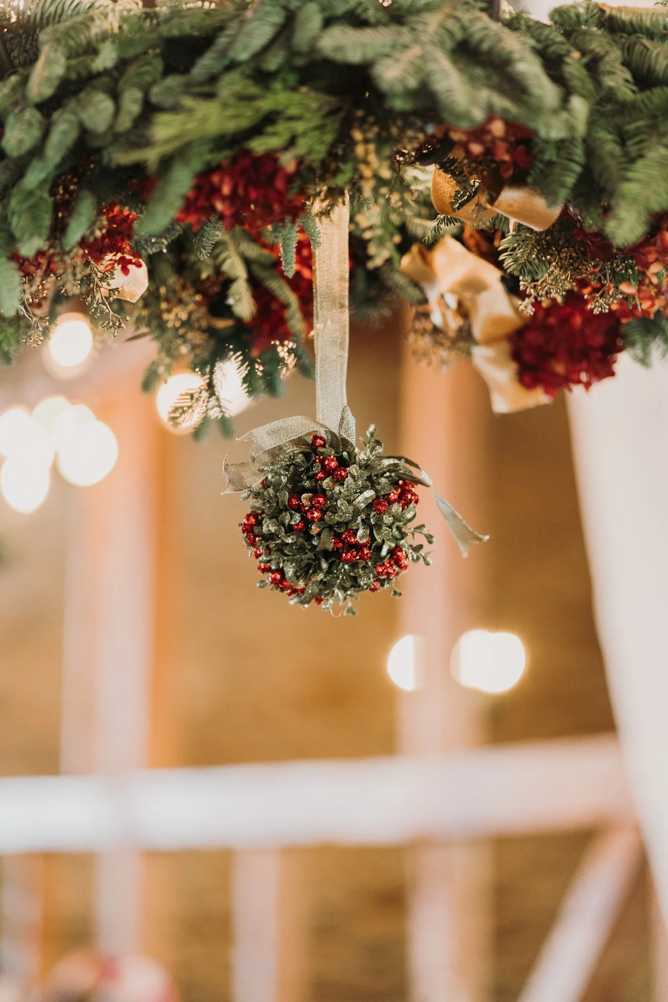 Close-up of a Christmas ornament hanging from a decorated tree with green pine needles and red and gold decorations, blurred lights in the background.