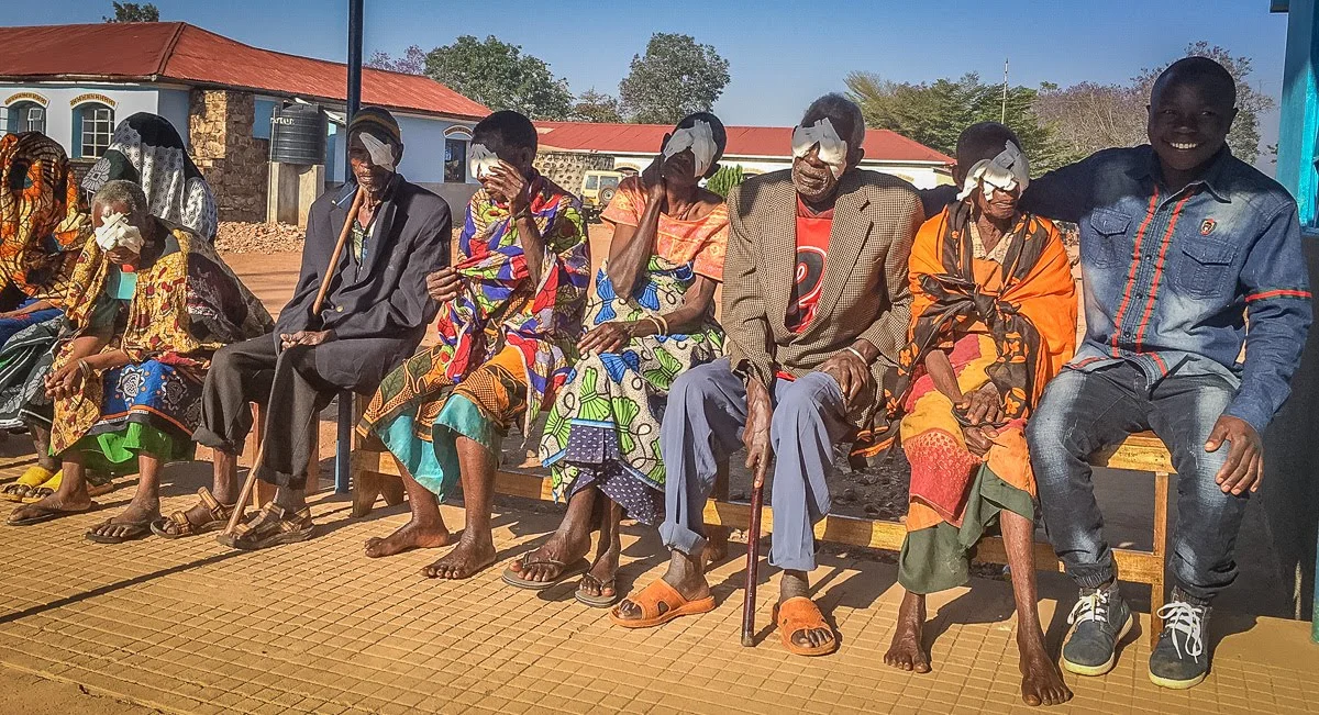 One of our youth, Kisuka, provides encouragement to the elderly as they await their turn for bandage removal.