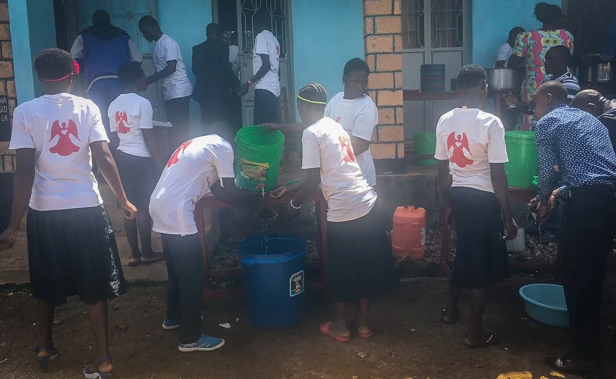 Our Youth preparing food (in the background), and Serving and Assisting the Elderly. Now that we have the well on site, there is an abundance of water for washing hands, cooking, and drinking at the gathering.