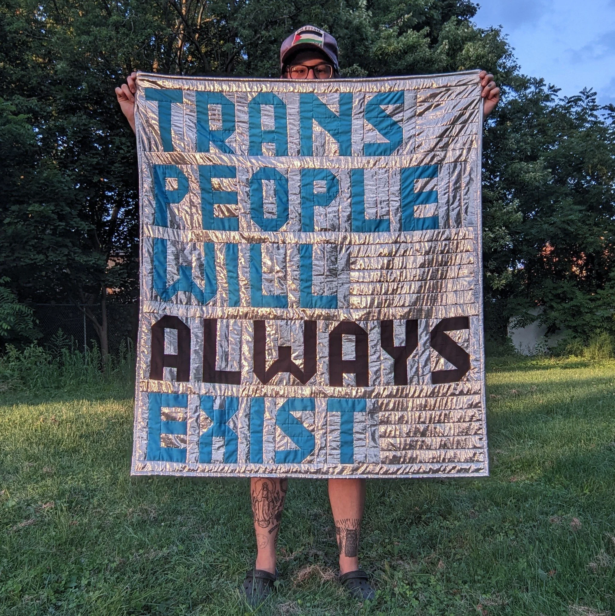 2025 47” x 41” made with thrifted fabric and surplus t-shirts no matter what you do to us, we're not going anywhere. as H. Melt wrote in There Are Trans People Here- "we are living in a new world. you can join us or become extinct" this silver fab