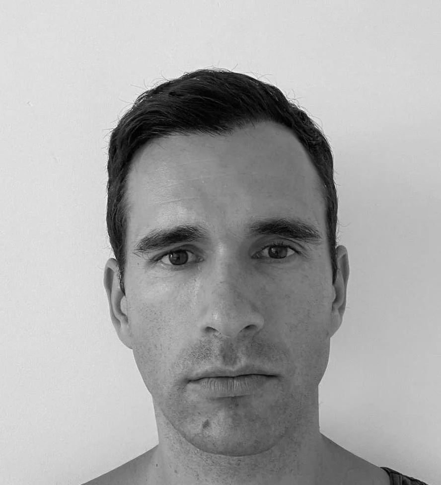 Black and white portrait of a man with short dark hair, looking directly at the camera against a plain light background.