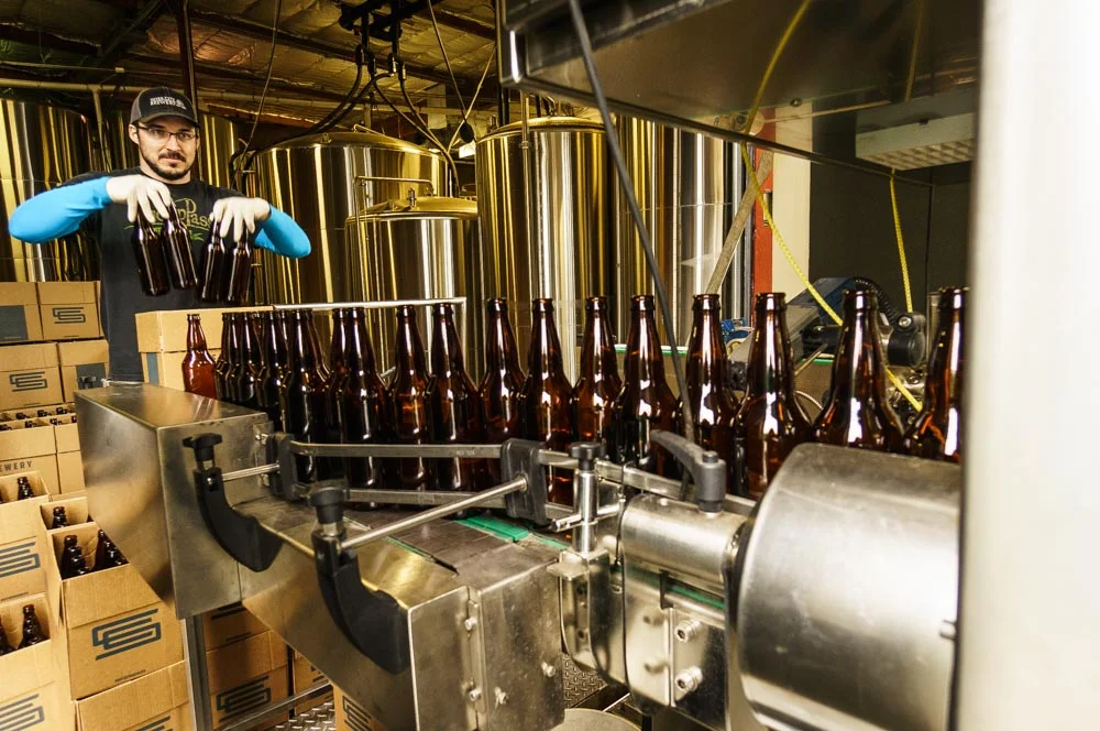 Silver City's Seth Hanson loads bottles into our Big Truck. These empty bottles will be labeled, interior rinsed, vacuum filled, crowned and rinsed, at a rate of nearly one bottle per second.