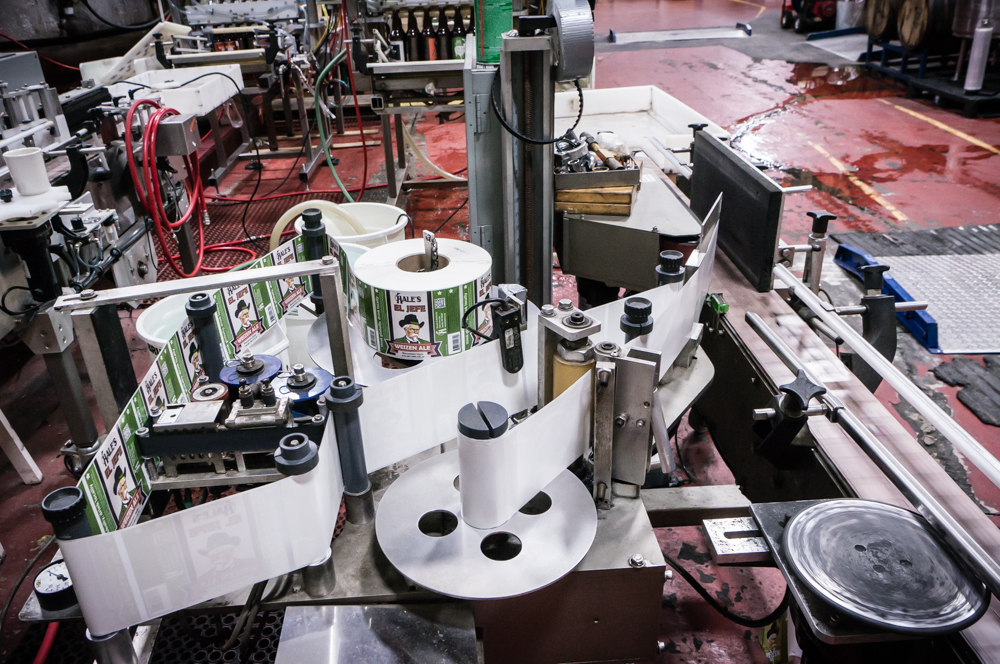 The Labeler spooled up and ready. Thermal ink date stamper on the left side. Empty bottles are fed into the conveyor belt on the right for labeling.