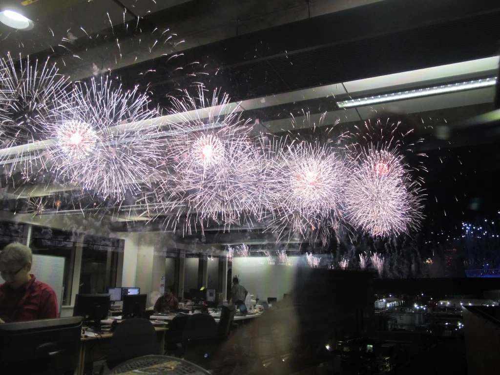 I took this photo of opening ceremony fireworks from our office in the main press center. I liked the reflection of our team (we have more than 50 staffers here) at work.