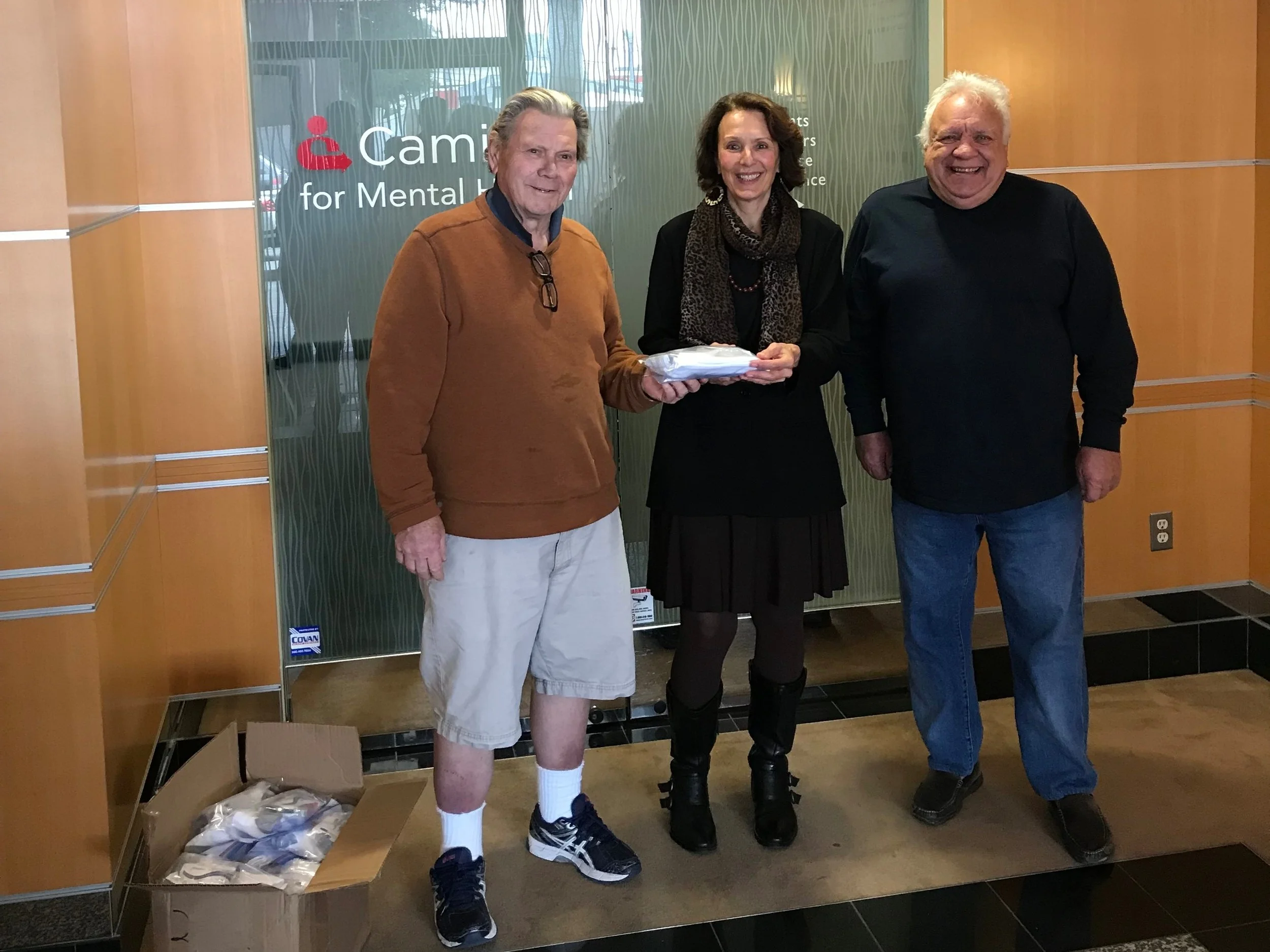 Roger Cutler (left) and Peter Cerri (right) of the Elks of San Mateo Lodge No. 1112 present Harriet Pecot, Caminar Director of Development (center), with 90 toiletry kits for Caminar clients.