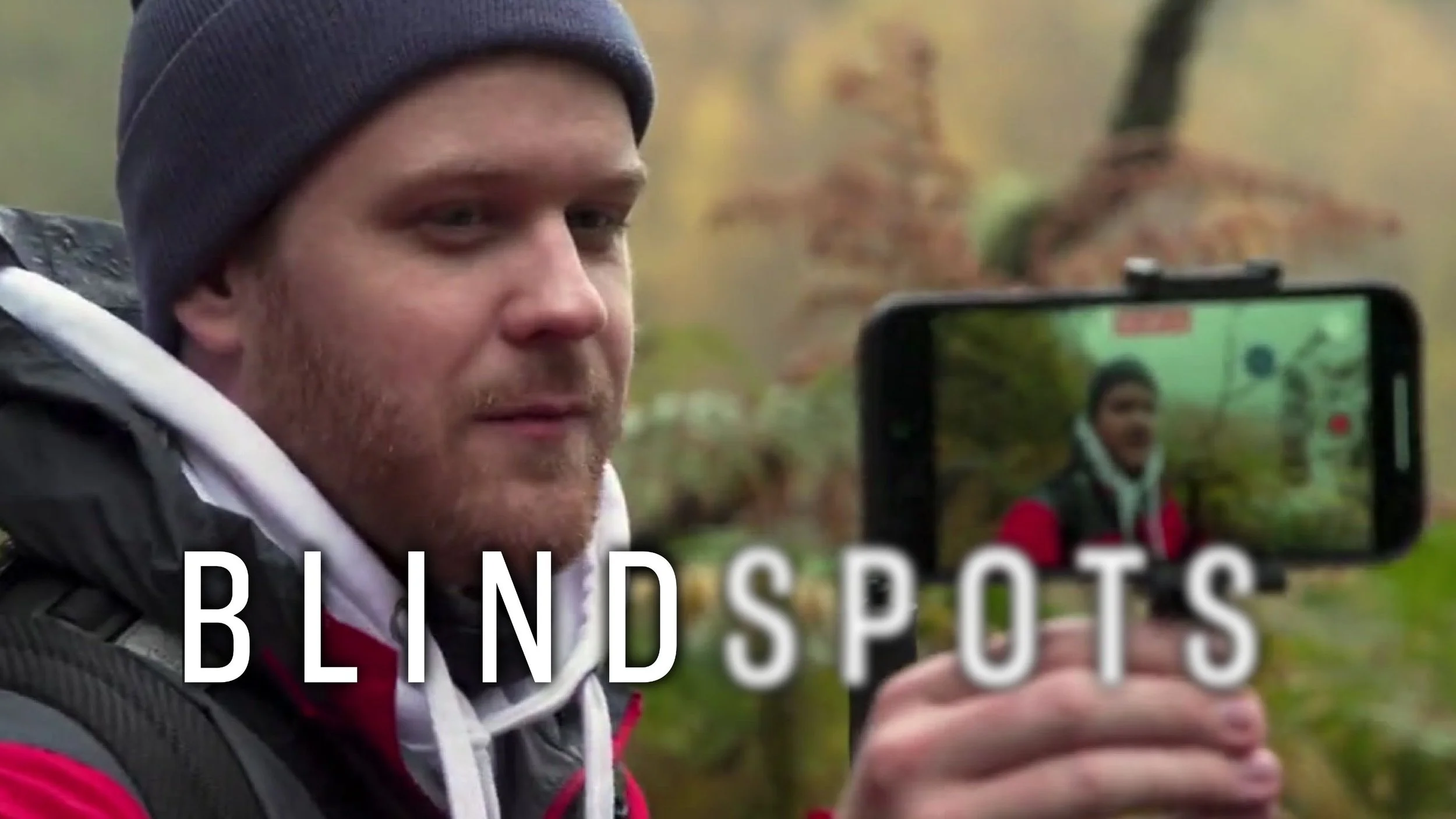 James Rath records himself on a smartphone hiking a lush trail in the rain. The Blindspots logo is overlaid. Spots is slightly blurred.