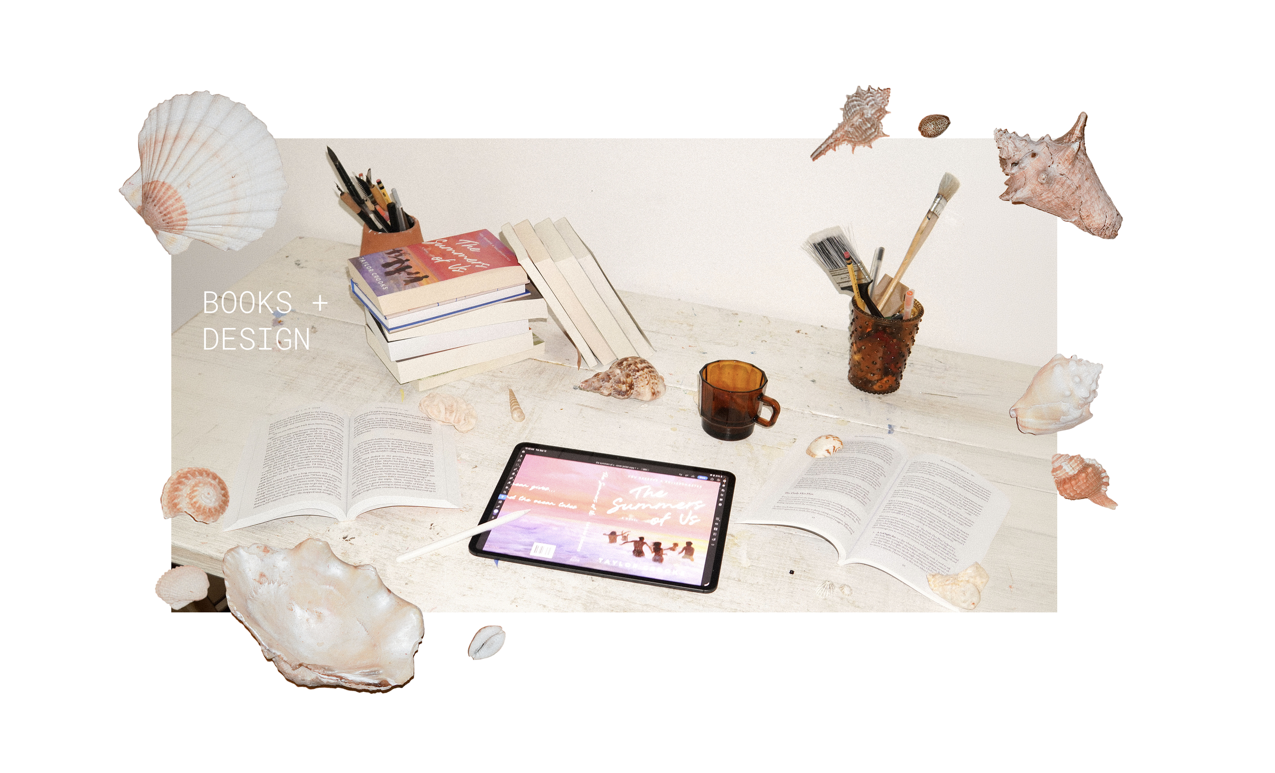 A workspace with books, seashells, a tablet, and writing utensils on a light wooden table.