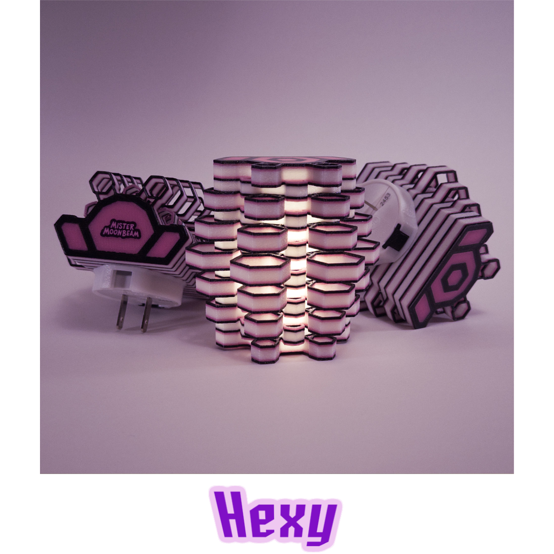 Three Hexy night lights in black and pink, one glowing, with plug prongs visible