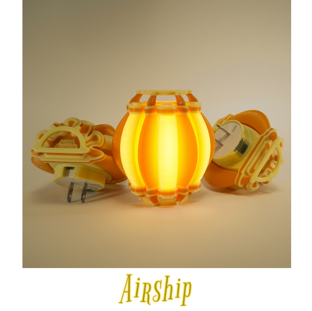 Three Airship night lights in yellow and orange, one glowing, with plug prongs visible