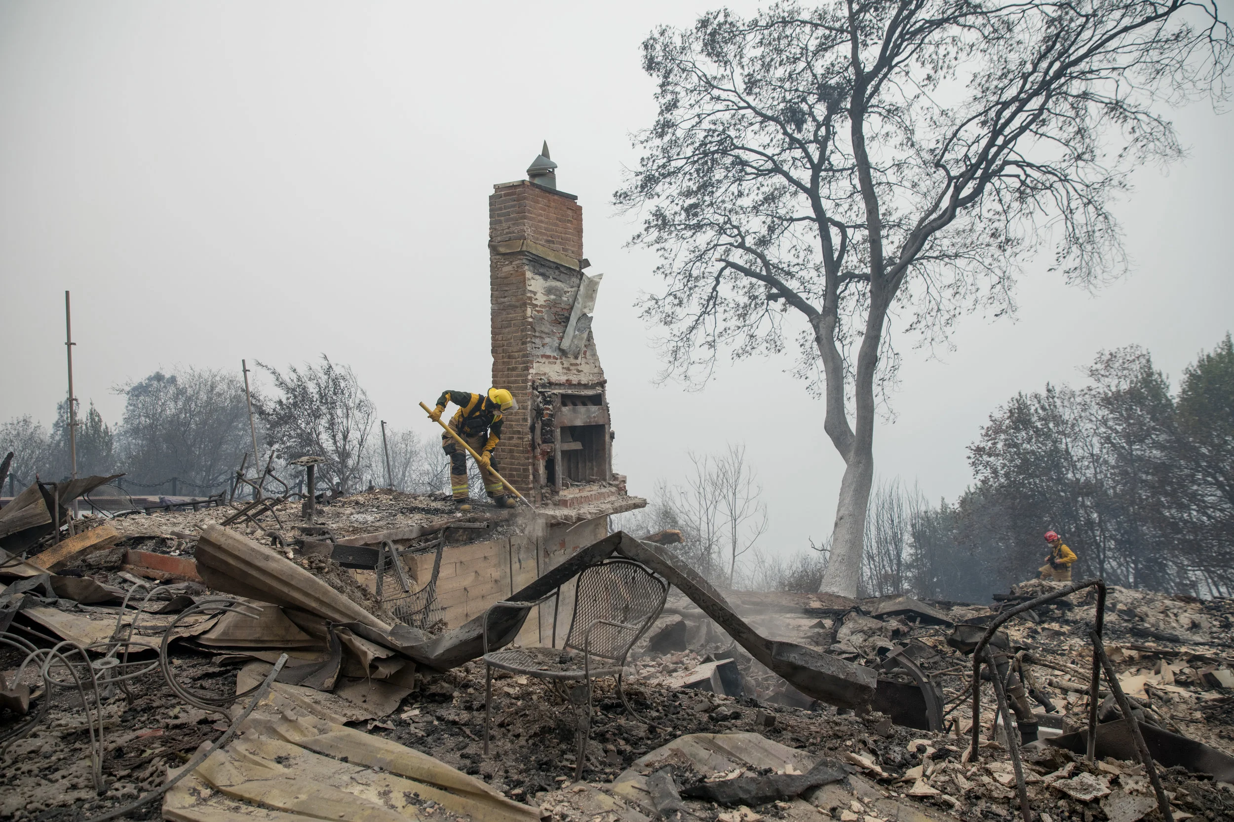 Firefighters from CAL FIRE clear away debris and try to knock out a chimney left standing before rescuers enter the scene in Paradise, CA — November 12th, 2018