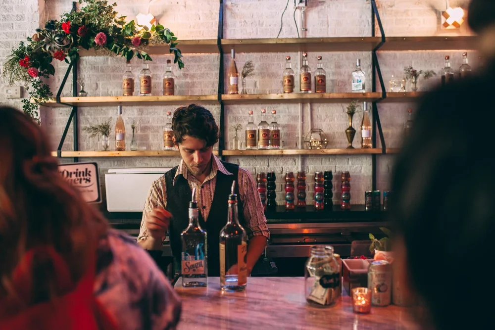A bartender at work in front of shelves of glassware