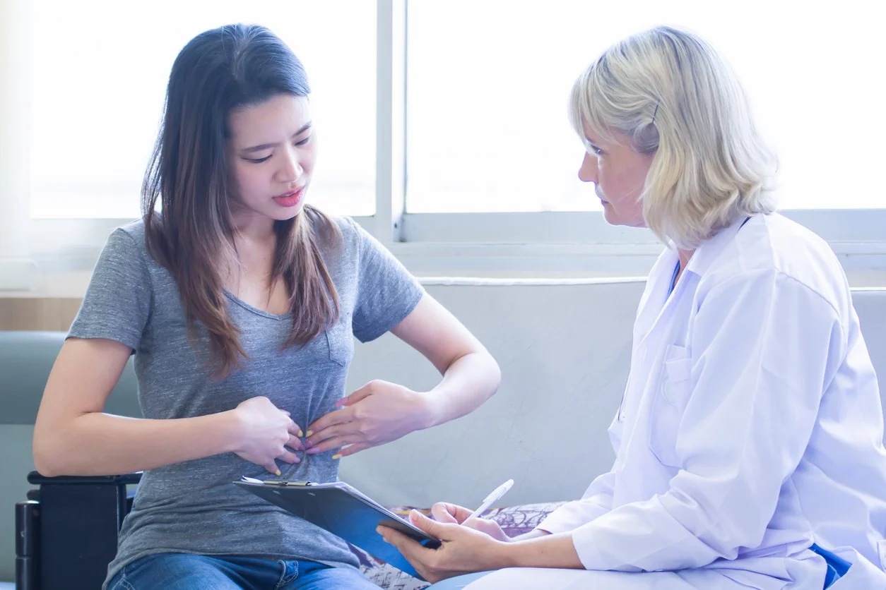 Young female pointing to her stomach while speaking to a nutrition expert