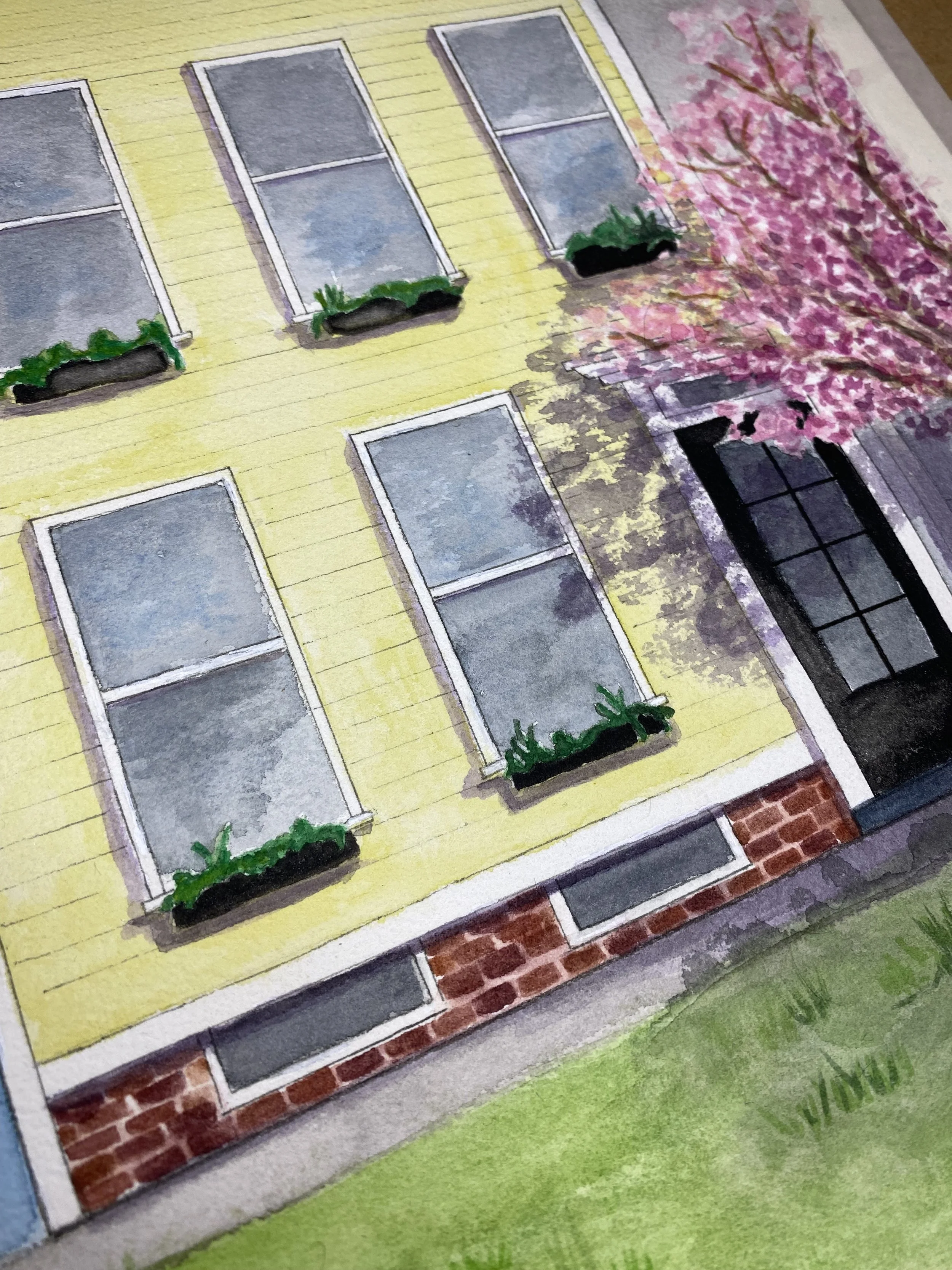 Illustration of a yellow house with six windows, three with flower boxes, and a pink blossoming tree next to it. The house has brick at the bottom and grass in front.
