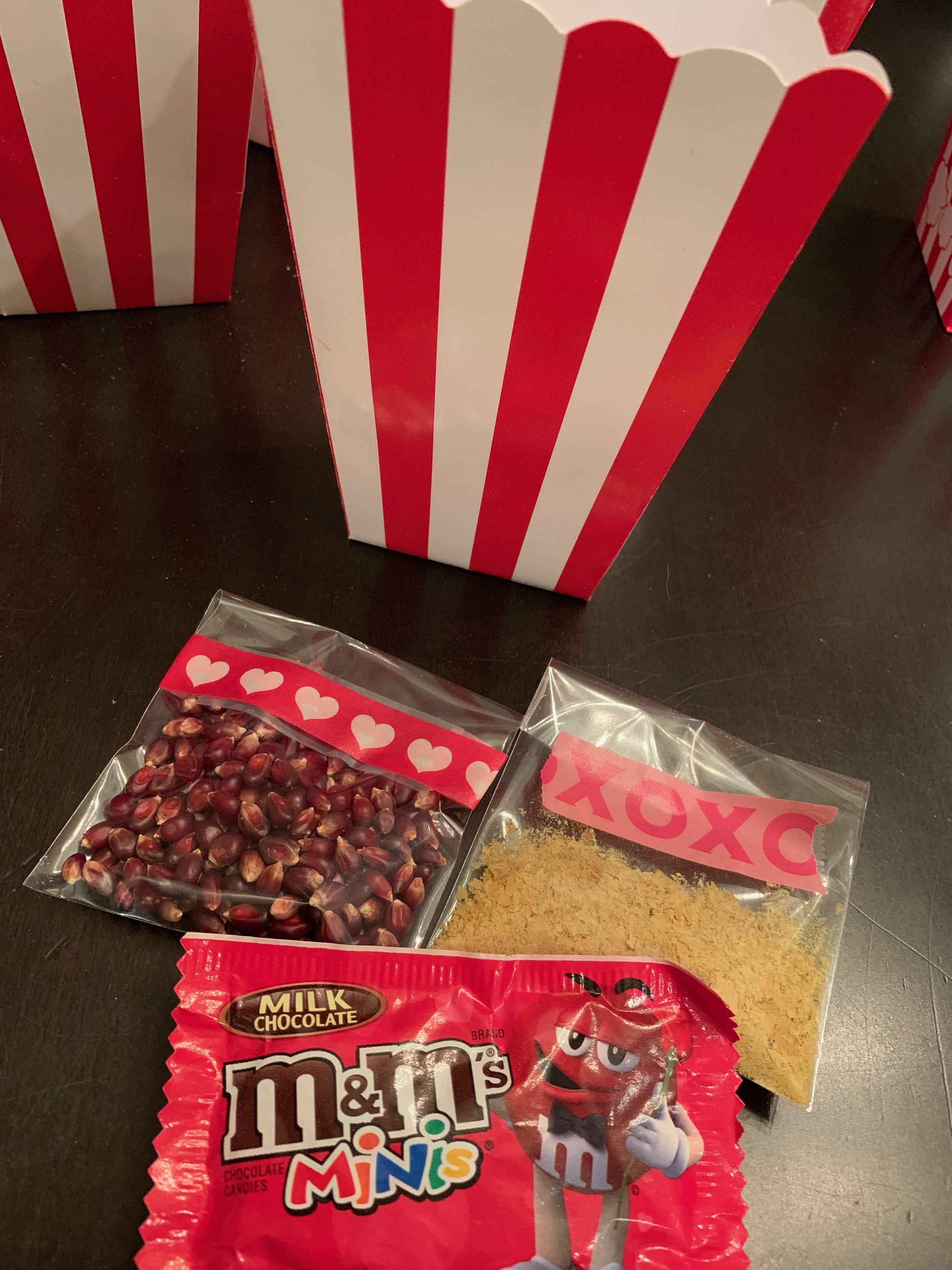 The kids and I like to pour our chocolate candy directly into our movie theater popcorn containers when we go to the movies. Specifically, Raisinettes. In this tiny kit made for one, besides the M&M’s, we have provided two tablespoons of Amish Red Kernel popcorn (bag with hearts) and 1 tablespoon of nutritional yeast*(bag with XOXO). For this single serving, just use 2 teaspoons of oil to pop the corn and when finished popping, top with butter, salt and sprinkle the entire packet of nutritional yeast over the cooked kernels. If you do not have coconut oil and/or Wilderness Family Naturals popcorn oil, just use whatever oil you prefer and butter.