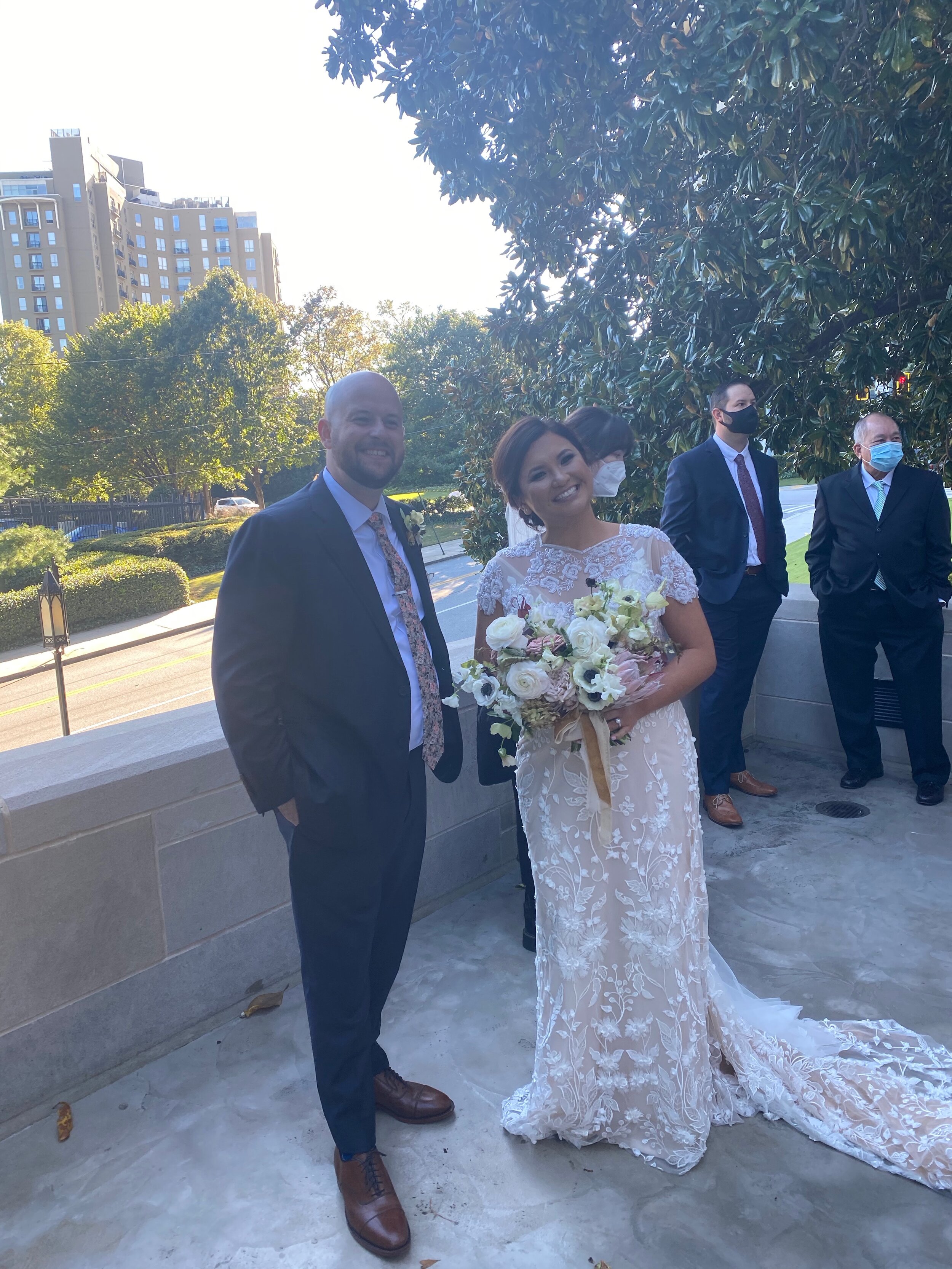 This couple right here - Nicholas (we call him “in the nick of time.”) and Pauline. Wedding photos capture a moment in time. In this photo we see a couple who is glad that the ceremony is over and next to them, guests wearing masks. When looking bac…