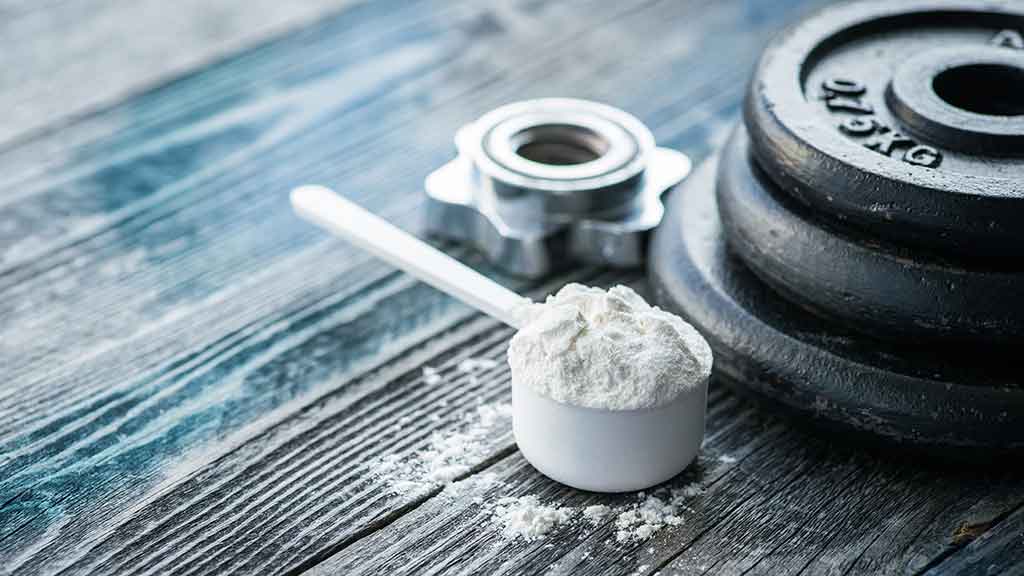 creatine in scoop with dumbell weights on table.jpg