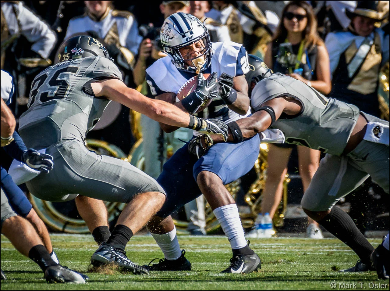 UNH kick returner Carlos Washington, Jr. (#26) winces as he is hit by CU safety Hasaan Hypolite (#12) and tailback Beau Bisharat (#35) during a kickoff return in the second quarter. Washington returned the ball to the UNH 10 yard line before being stopped.