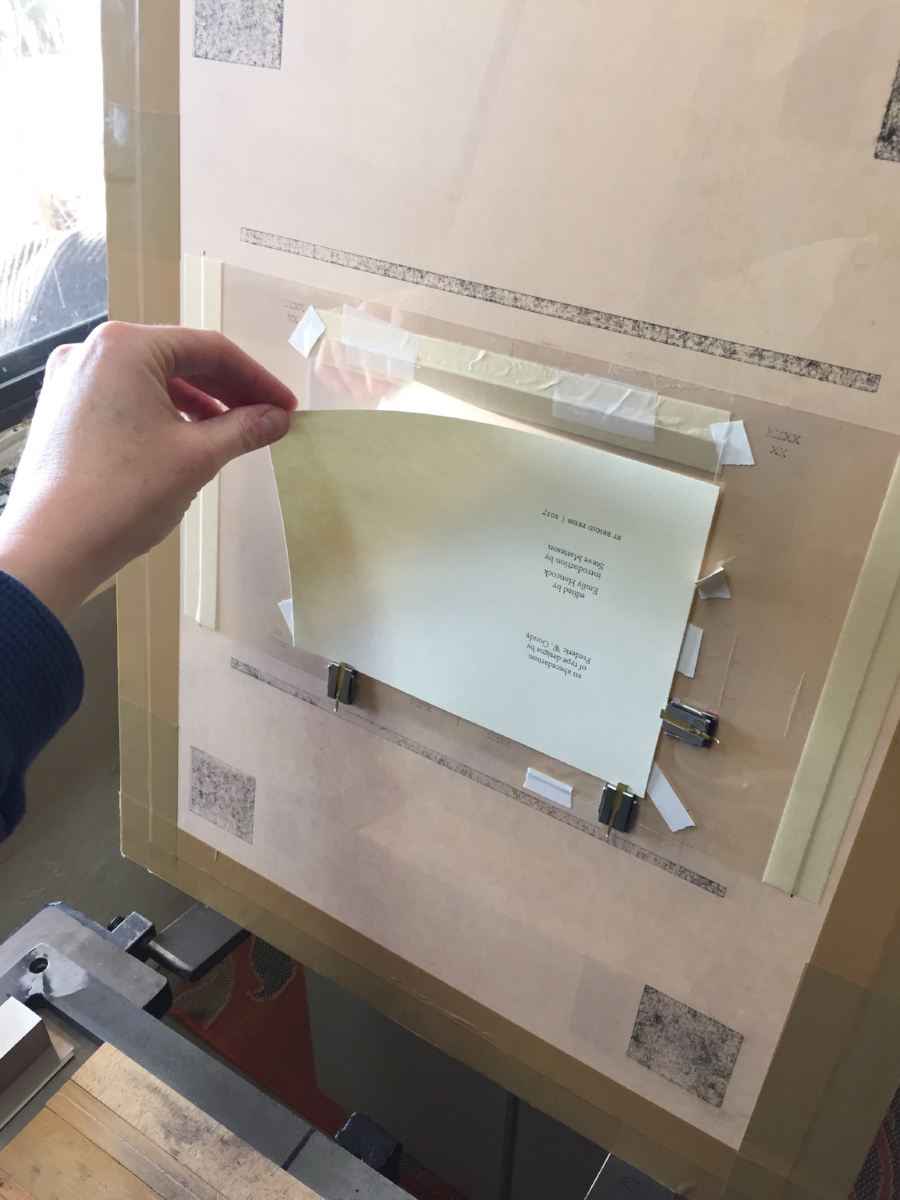  The first step is to place, or "hang," the sheet of paper-to-be-printed on the tympan. You can see the little metal guides that keep the page in the correct spot. (You can also see the words in black ink that I printed earlier in the week.) 