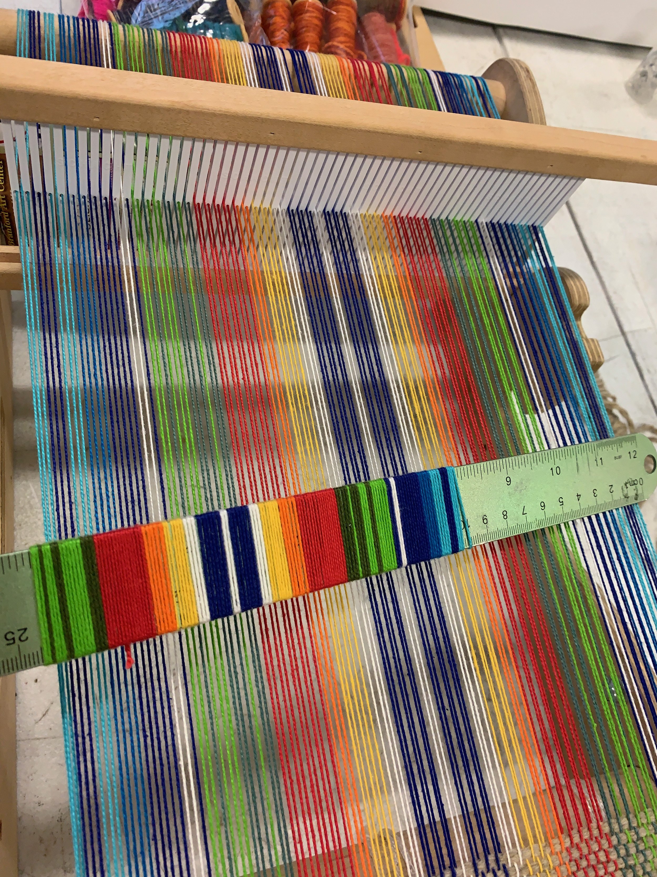 Colorful weaving loom with yarn and a measuring tool.