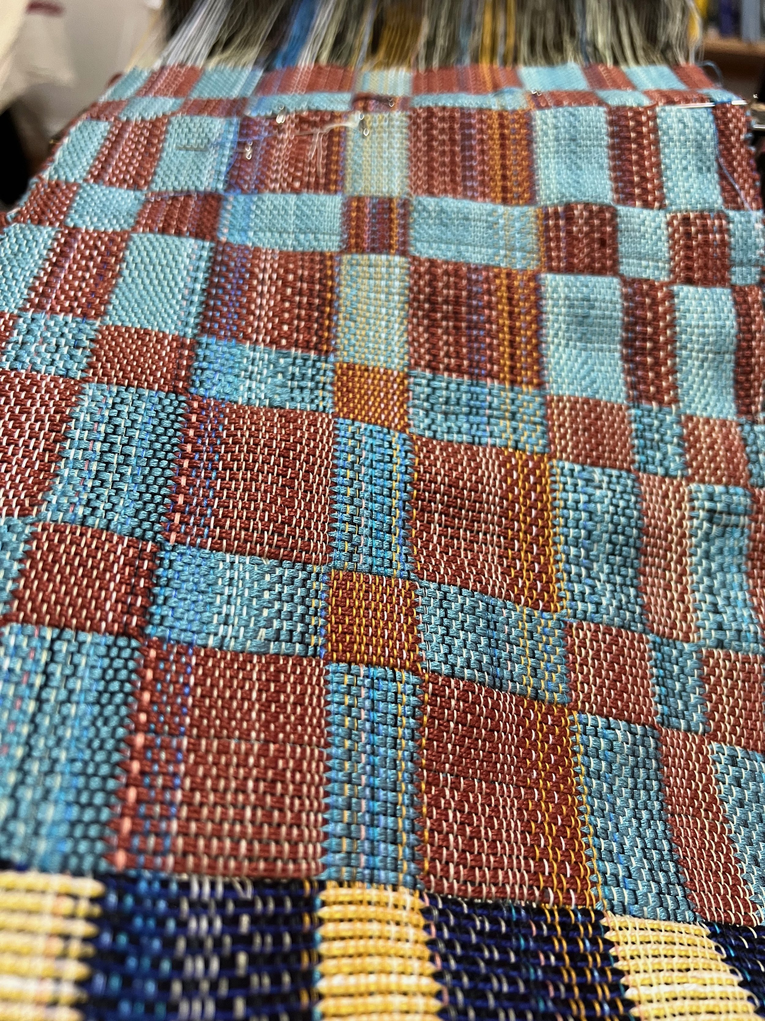 Colorful woven textile with red and blue checkered pattern on a loom