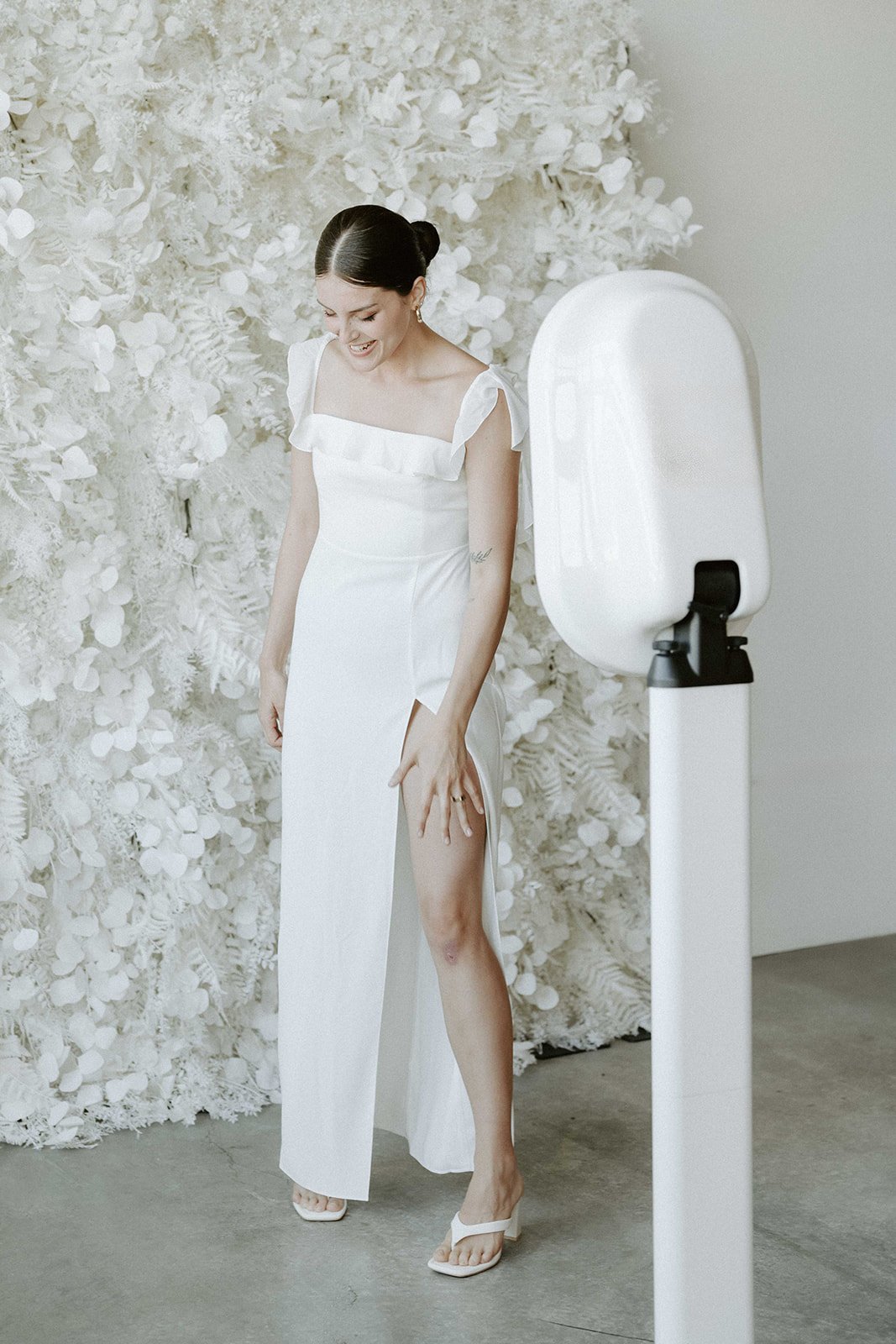 Woman in white dress posing near floral backdrop and photo booth