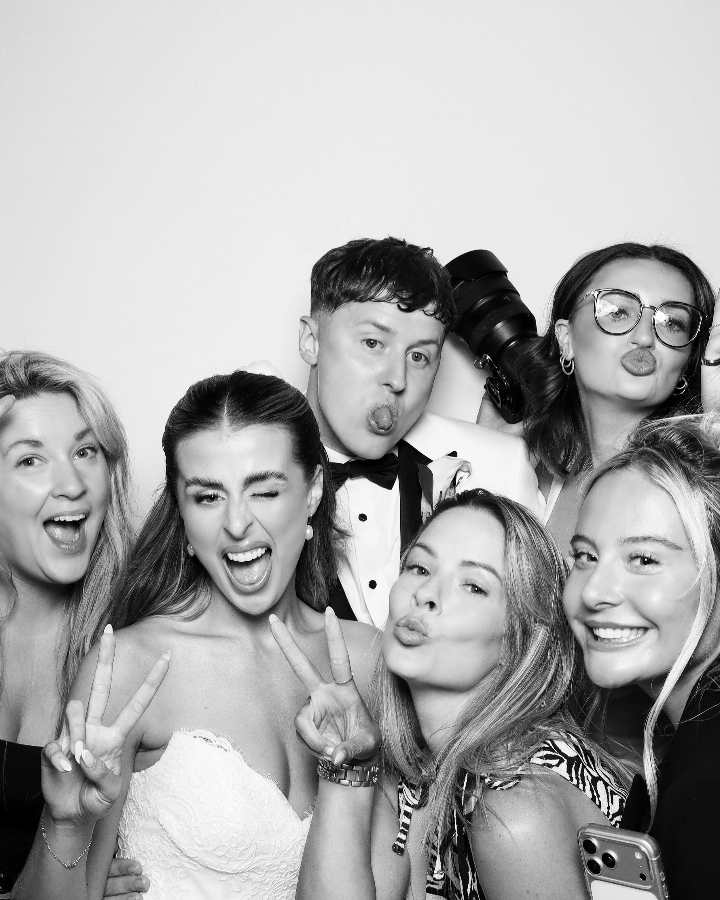 Group of young women taking selfies, making playful faces, and holding peace signs in a black and white photo.