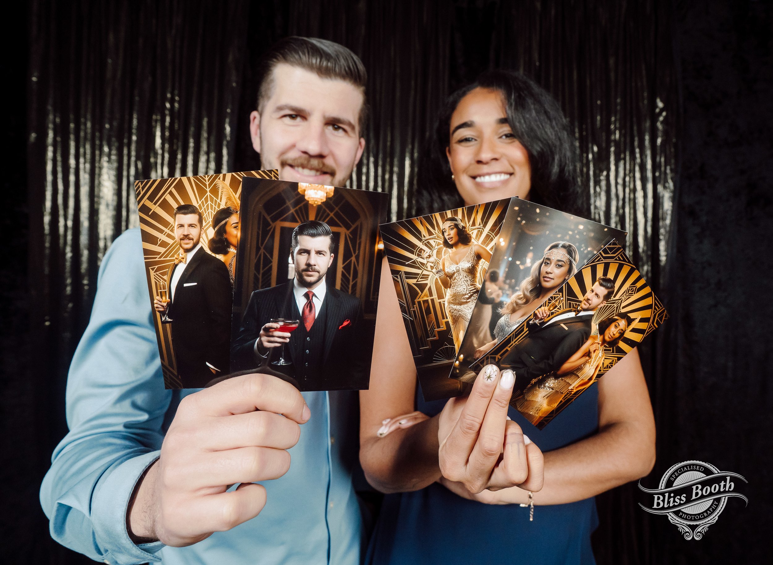 A man and a woman are holding up decorative photos at a photo booth with a dark curtain background. The man is wearing a light blue shirt and the woman is in a dark dress, both smiling.