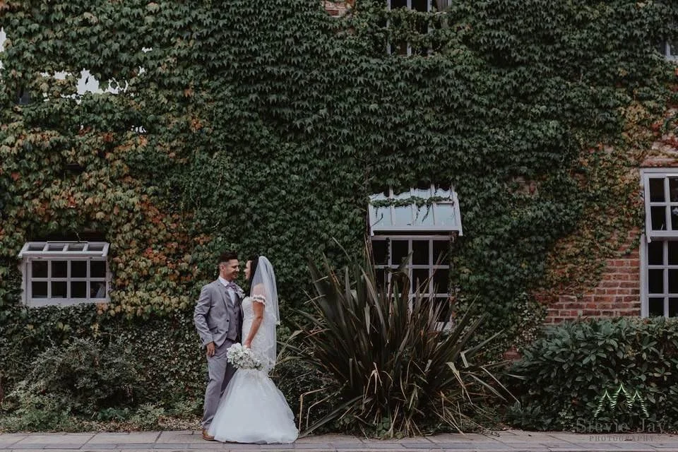 Bride and groom outside Lazaat Hotel in Hull, standing by an ivy-covered wall in the venue’s landscaped garden