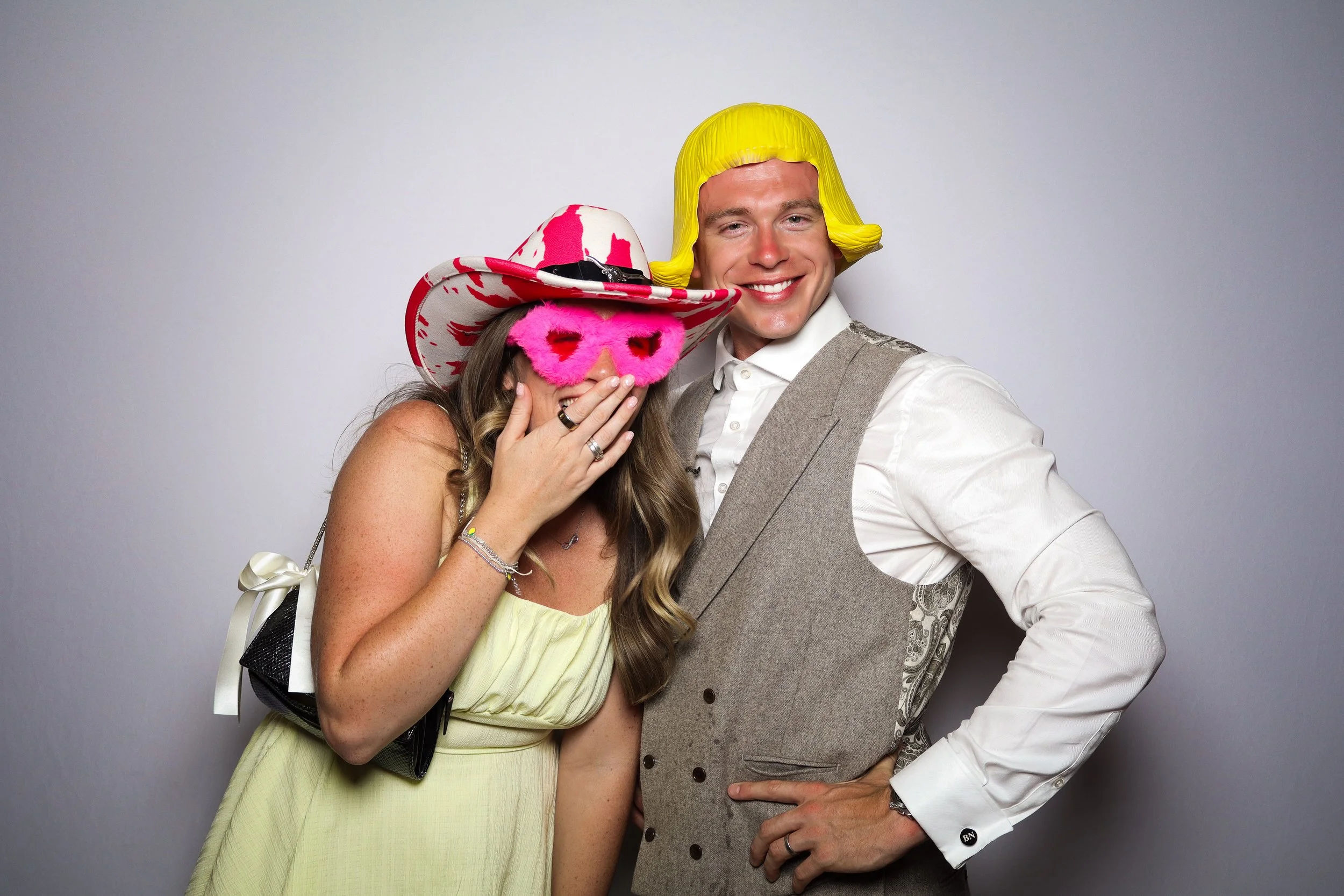 Couple wearing fun props and taking a selfie in a wedding photo booth.