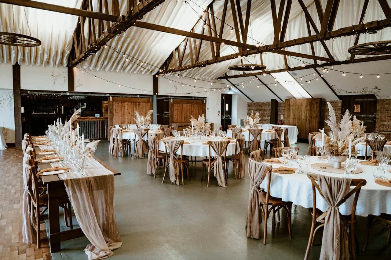 Bright wedding reception at Beverley Barn in East Yorkshire, featuring exposed beams, round tables and modern rustic décor.