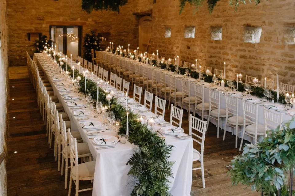 Long banquet-style wedding table at Hooton Pagnell Hall with candles, greenery and rustic stone walls.