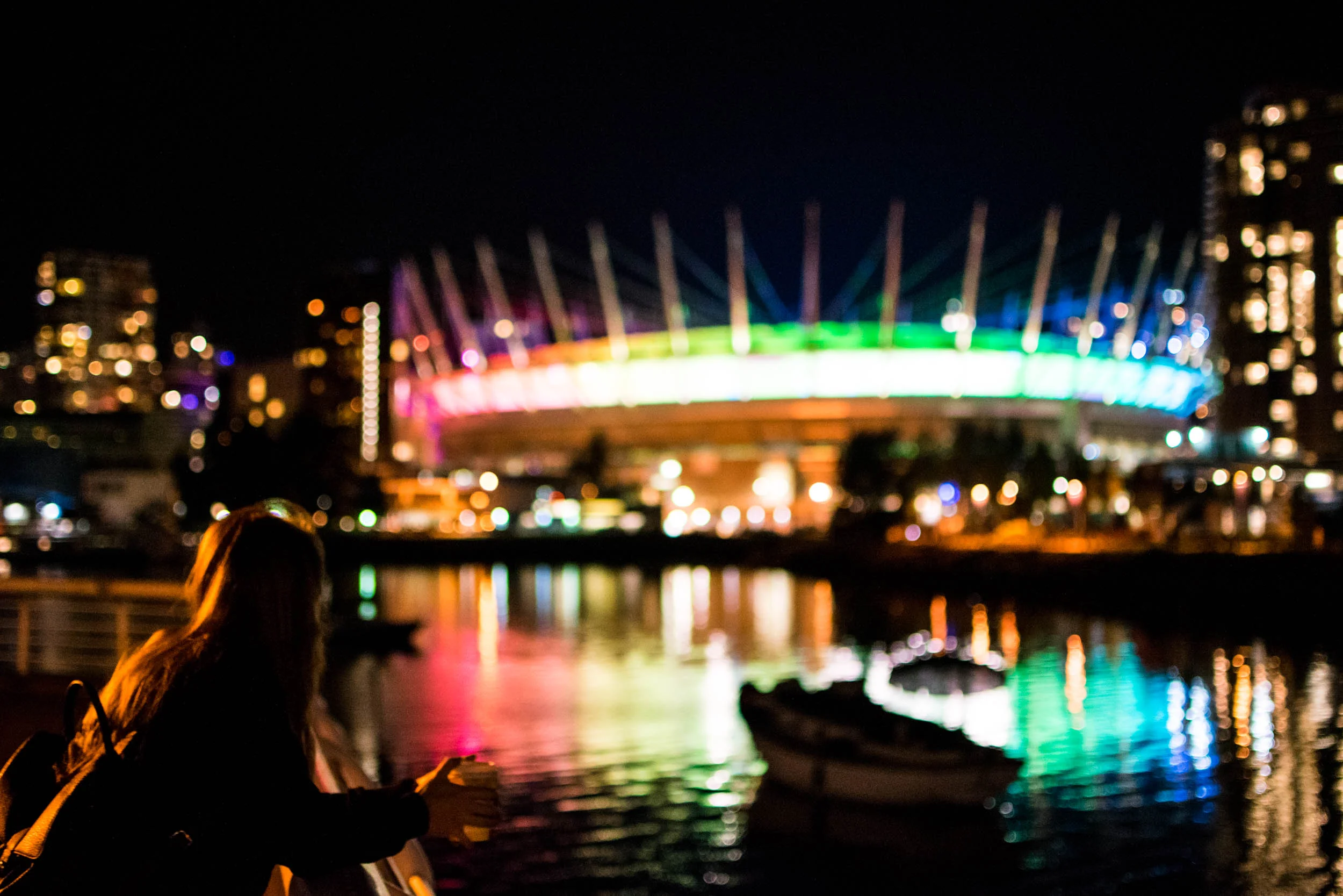 Woman looking at BC Place at night in Vancouver's False Creek, stopping on the seawall.