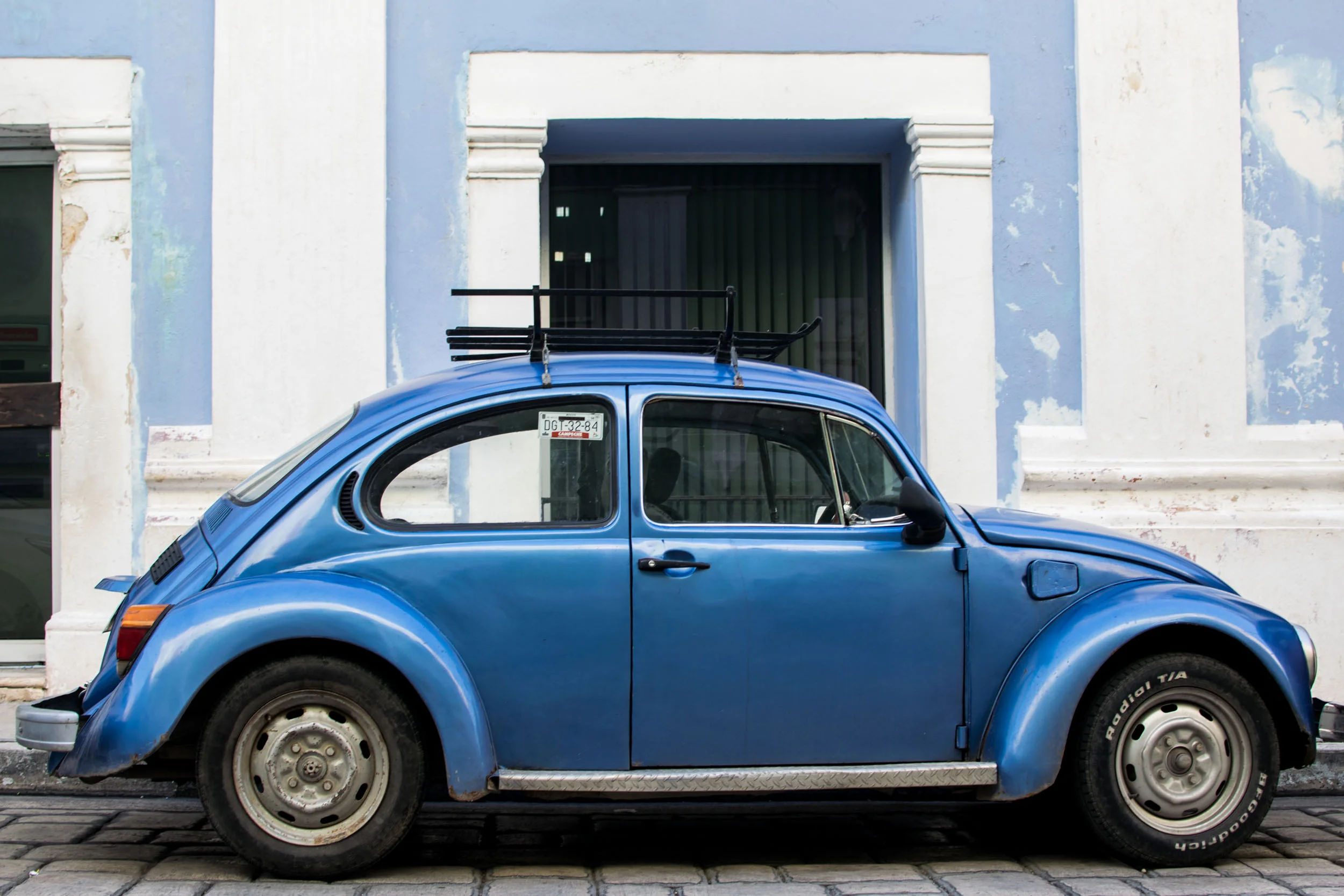 Blue VW Beatles against a pastel blue wall in Campeche, Mexico.
