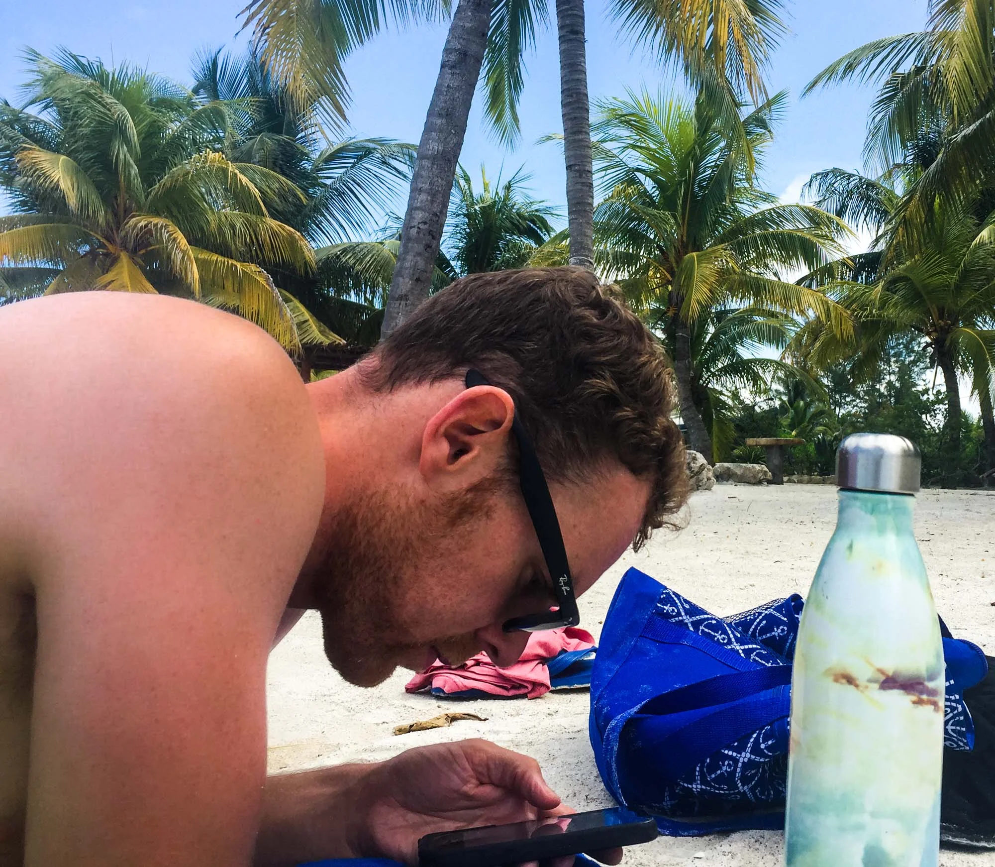 Man looking at iPhone to book flights on beach in Mexico.