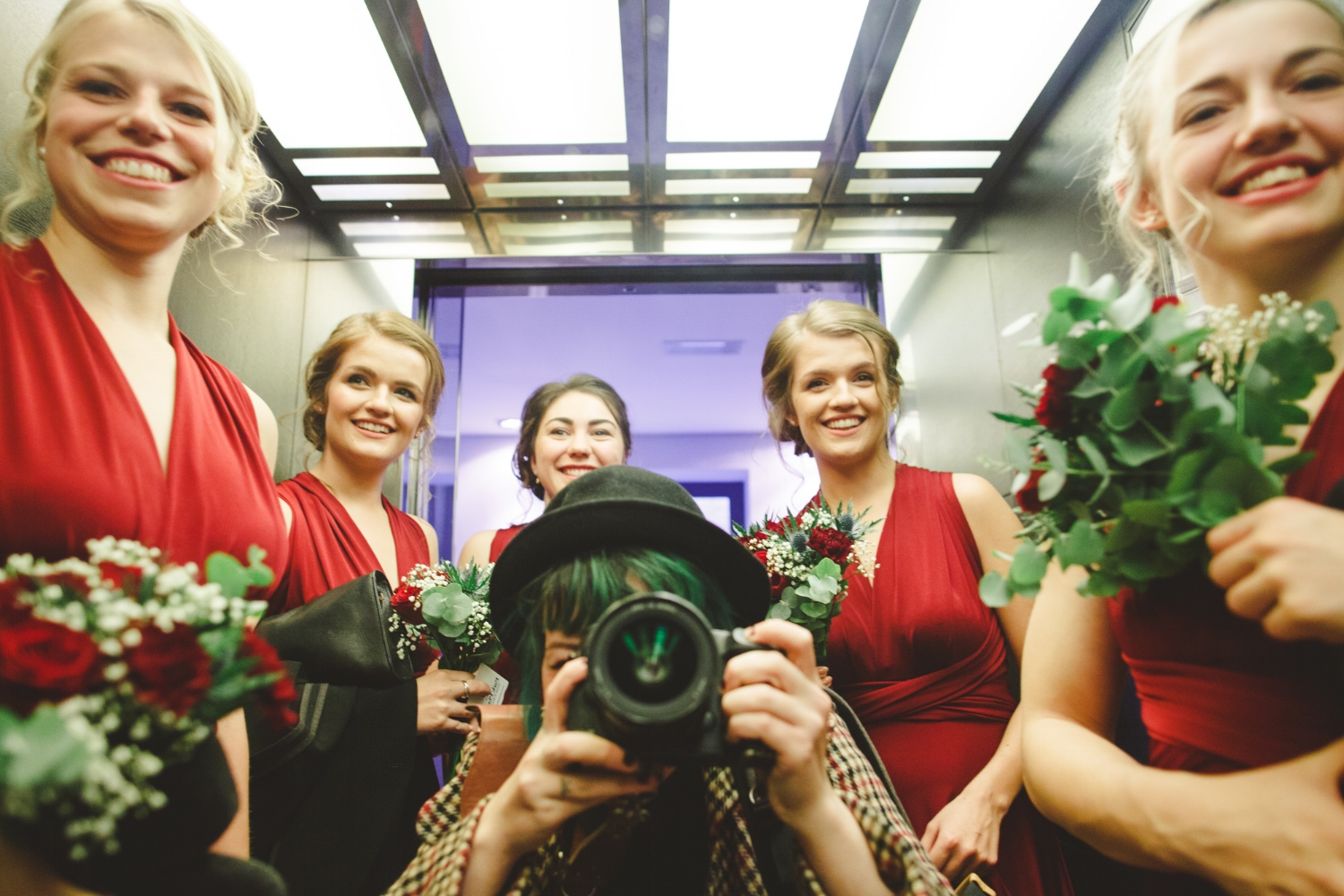 Alternative wedding photographer with bridesmaids in red dresses taking photograph
