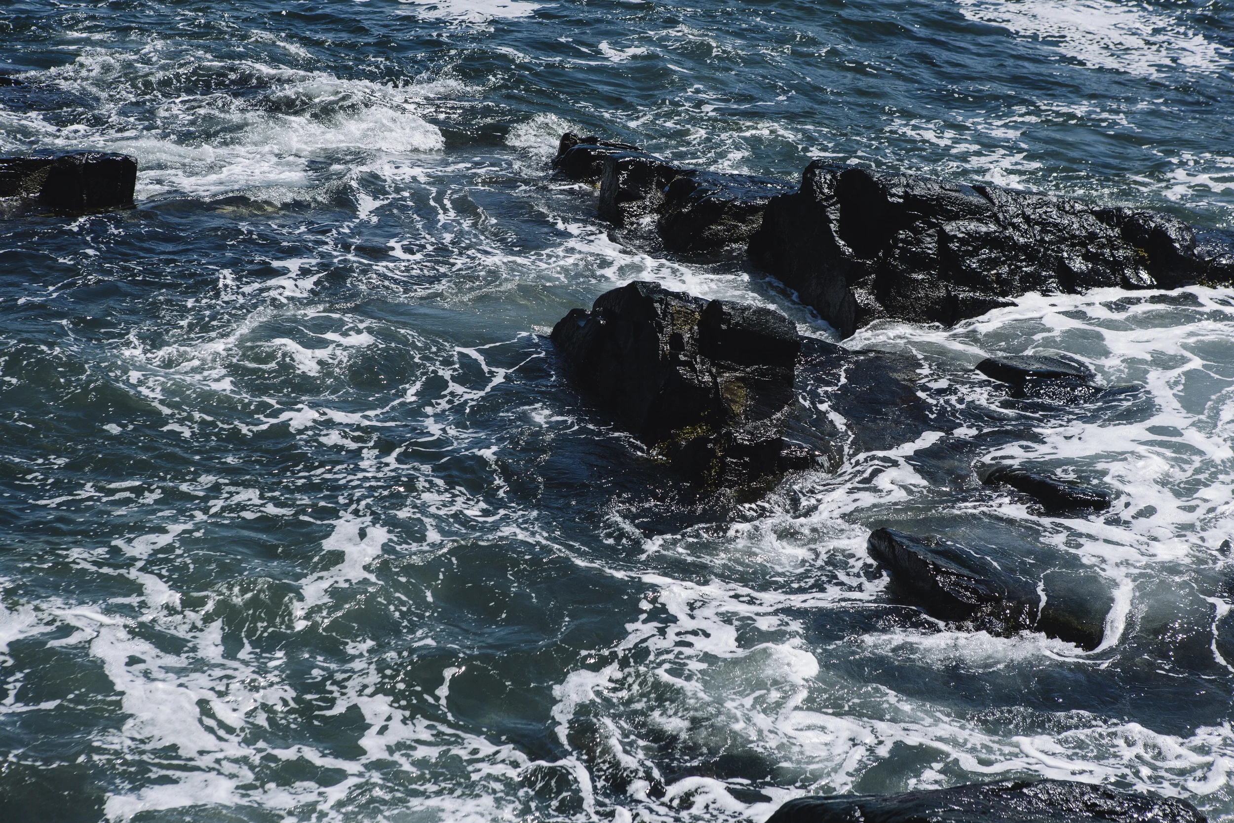 Ocean waves crashing against black rocks.